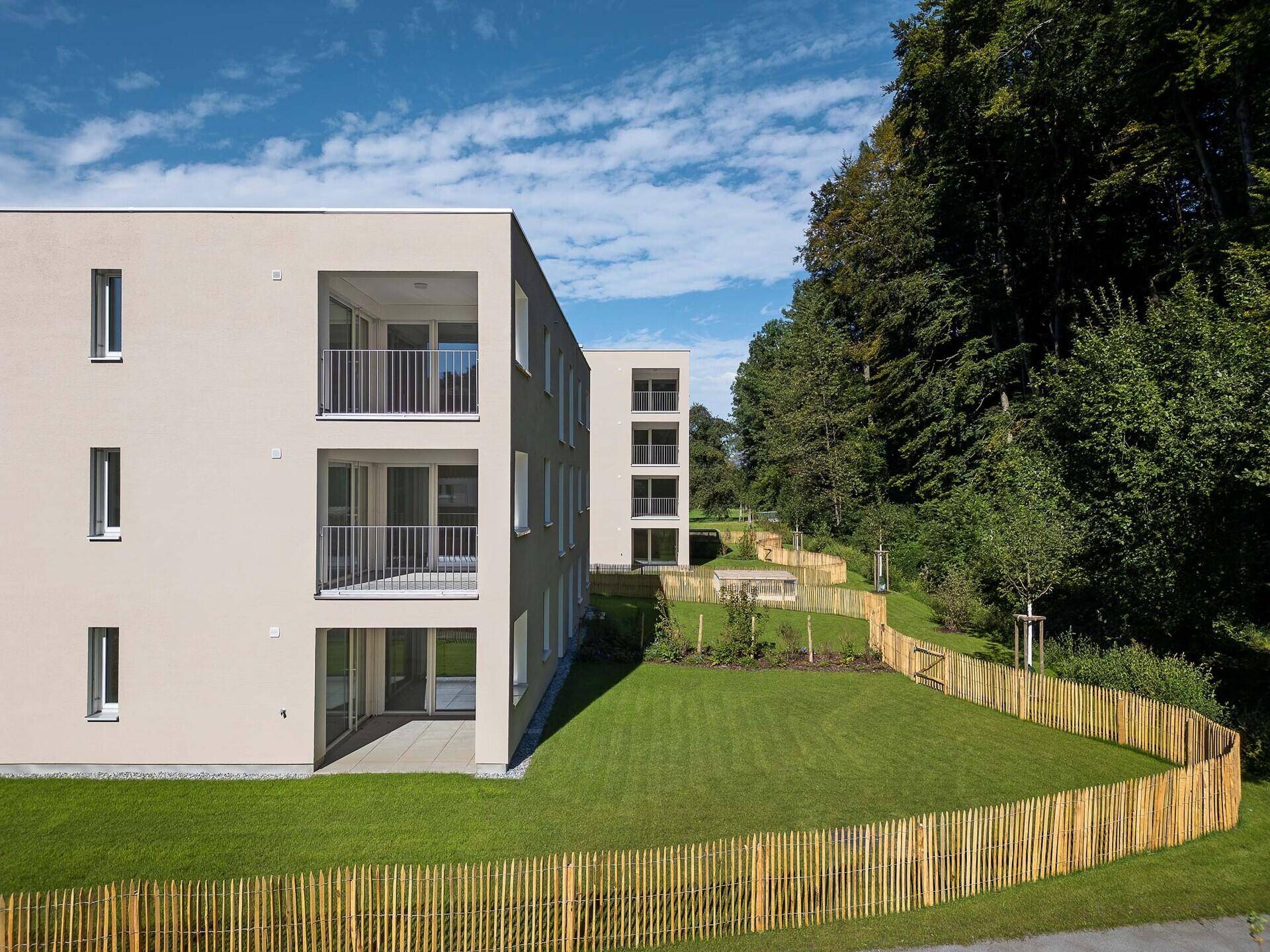 Moderne Wohngebäude mit Balkonen und Terrassen, umgeben von einem bewaldeten Hang.