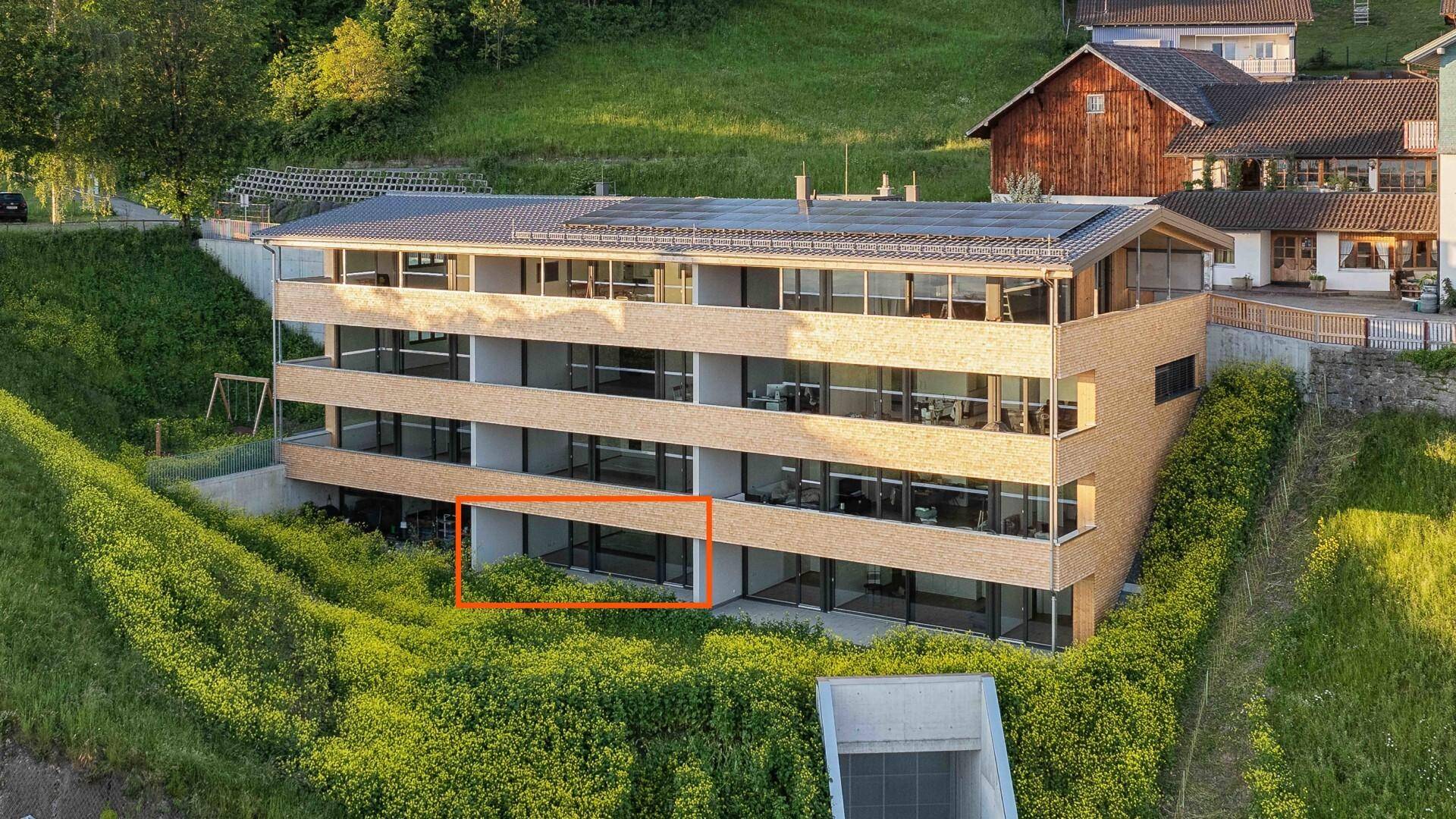 Modernes Apartmentgebäude in Hanglage mit Solaranlage auf dem Dach und grüner Umgebung.