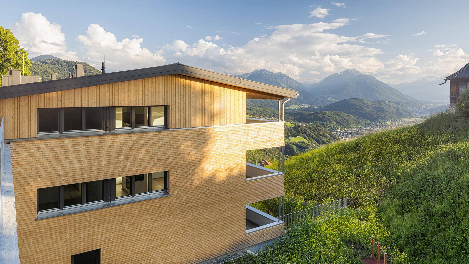 Oberer Teil des modernen Gebäudes mit Balkonen und atemberaubendem Blick auf die umliegende Berglandschaft.