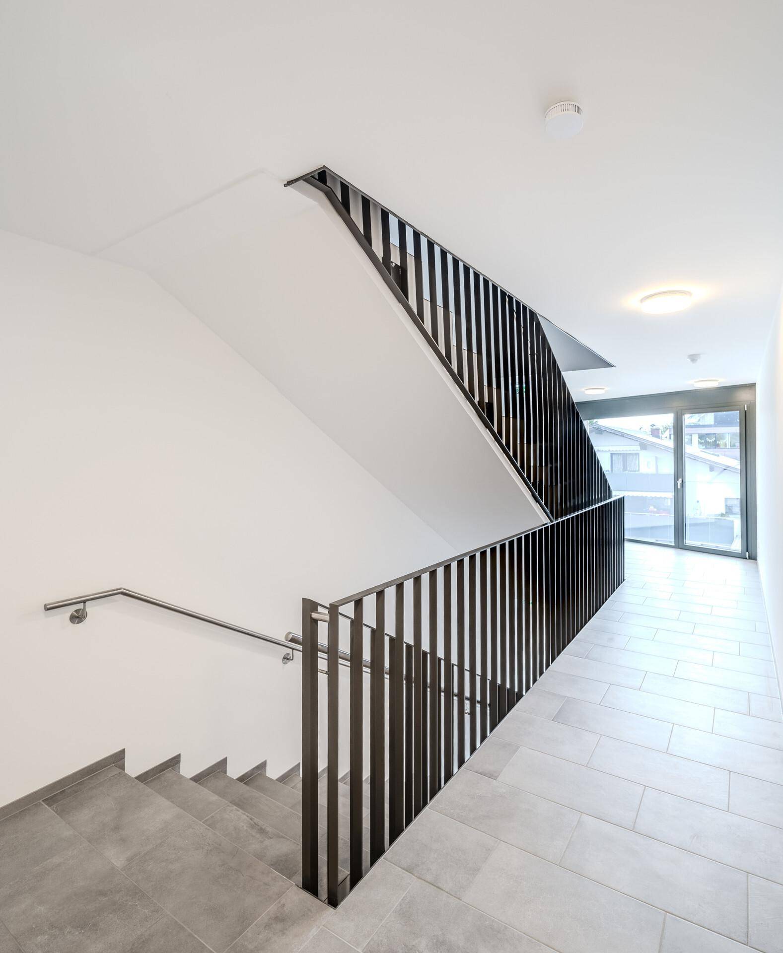 Modernes Treppenhaus mit grauen Fliesen und eleganten schwarzen Metallgeländern in einem Mehrfamilienhaus.