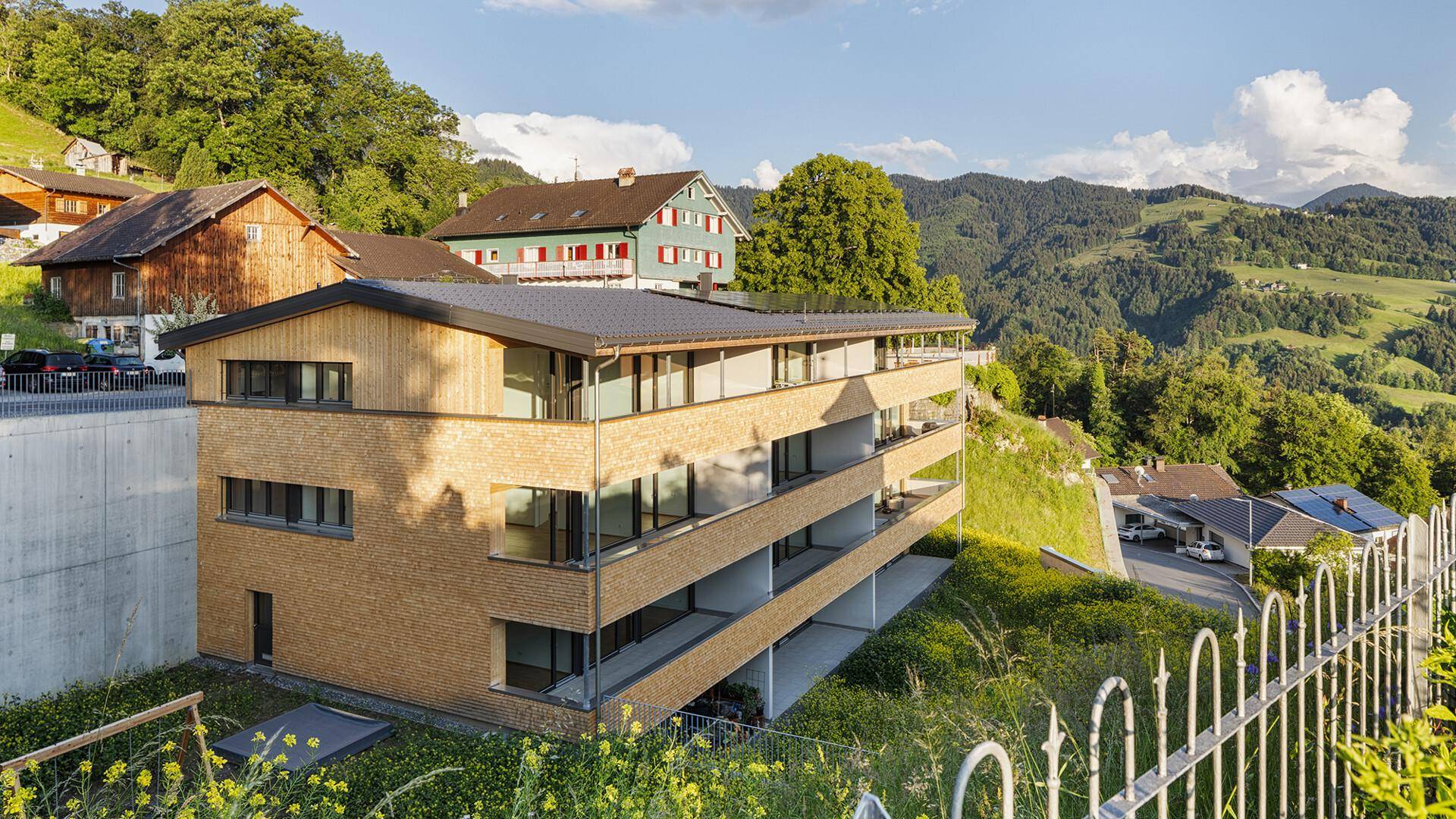 Modernes Wohngebäude in ländlicher Umgebung mit Bergblick und angrenzenden traditionellen Häusern.