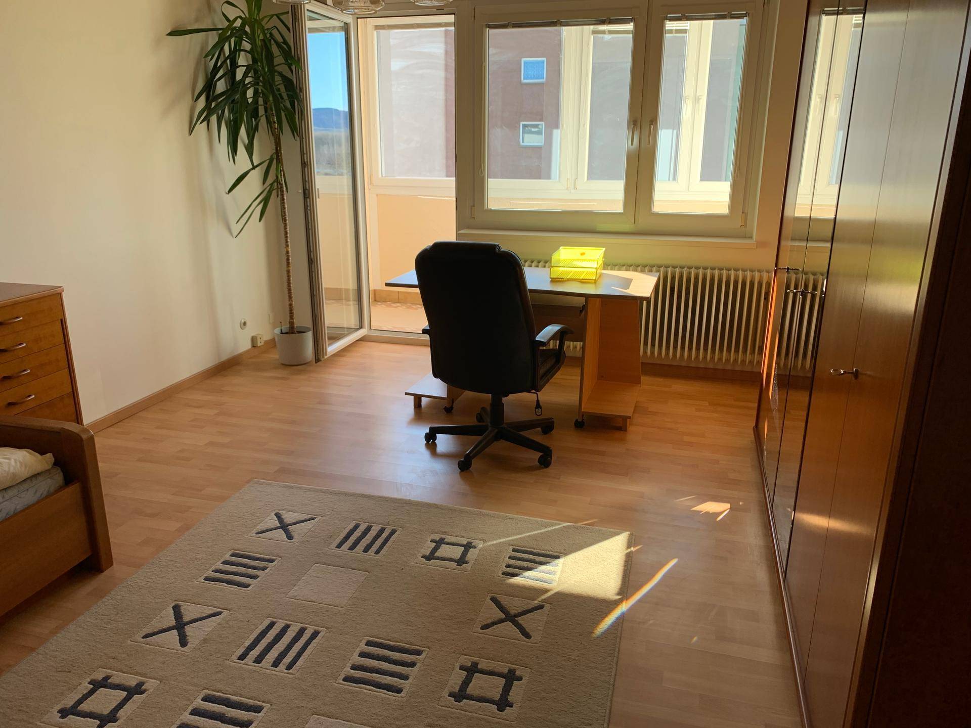 Helles Schlafzimmer mit Holzboden, Schreibtisch und direktem Zugang zu einem Balkon.