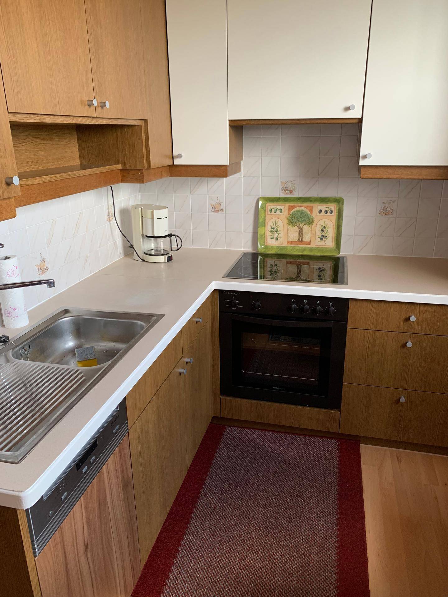 Funktionale Küche mit hellen Holzschränken, integriertem Backofen und Kochfeld.