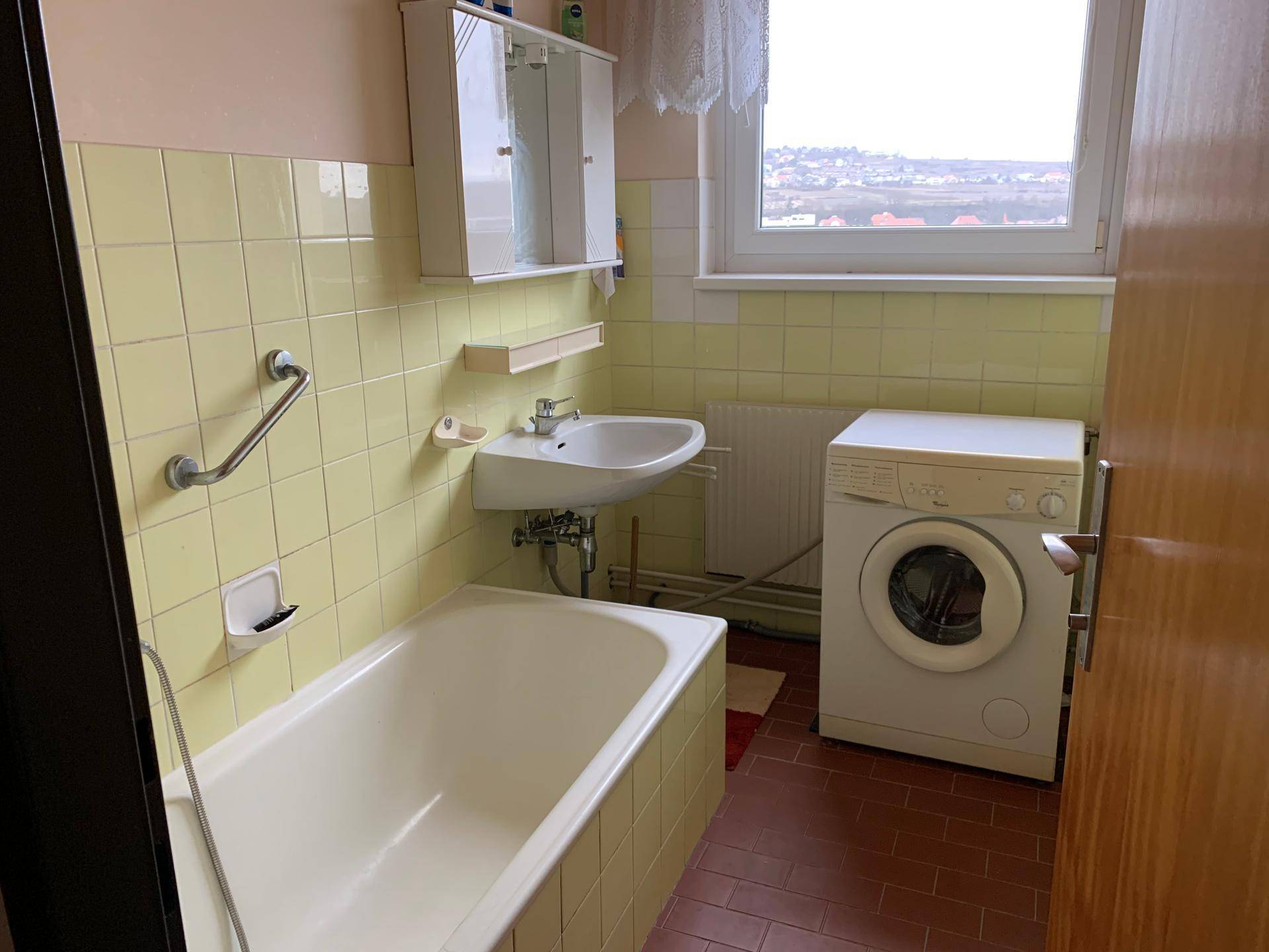 Badezimmer mit Badewanne, Waschbecken und einer Waschmaschine, hell gefliest.