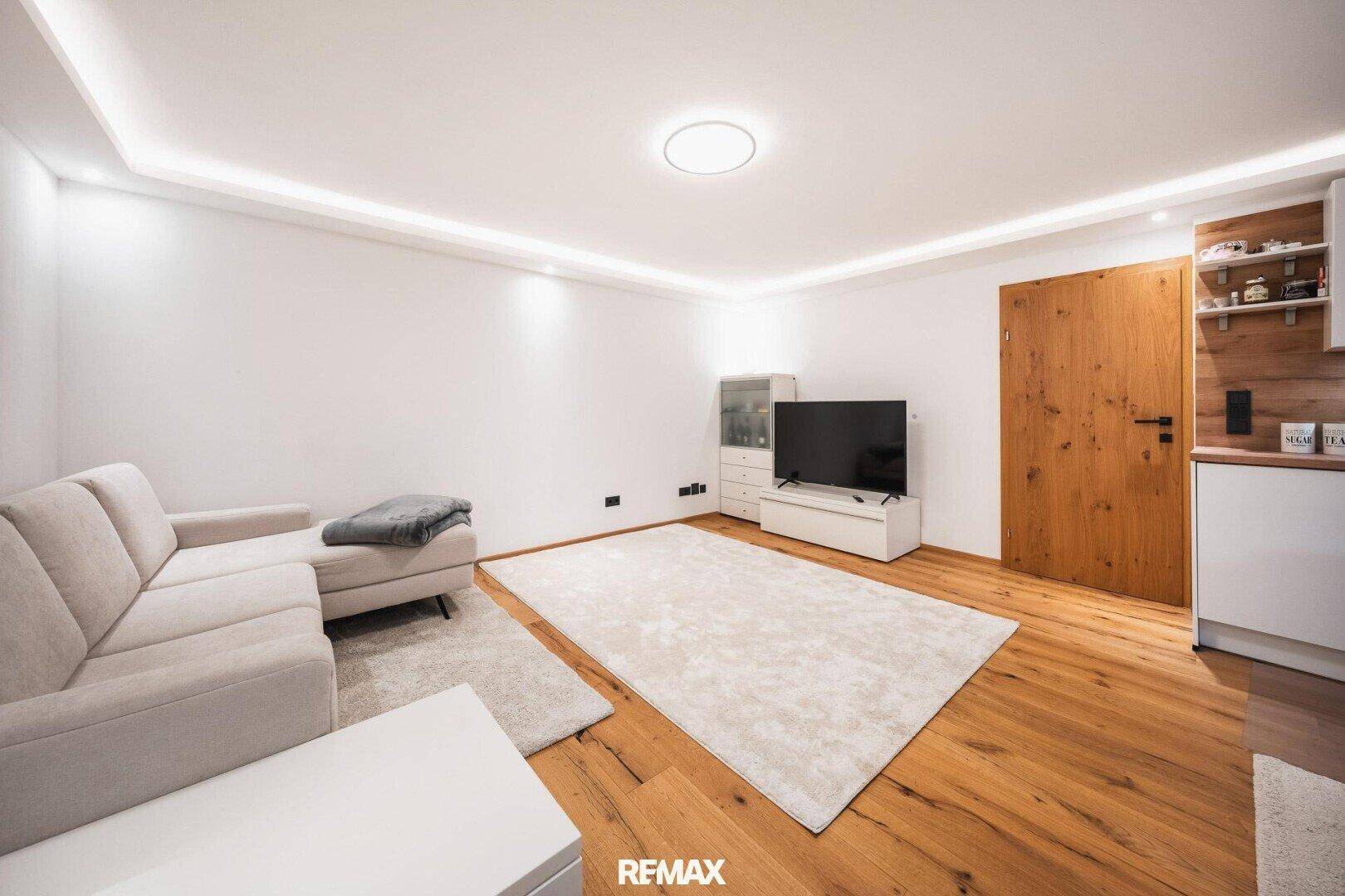 Gemütlicher Wohnbereich mit beigem Sofa, Fernseher und Holzboden.