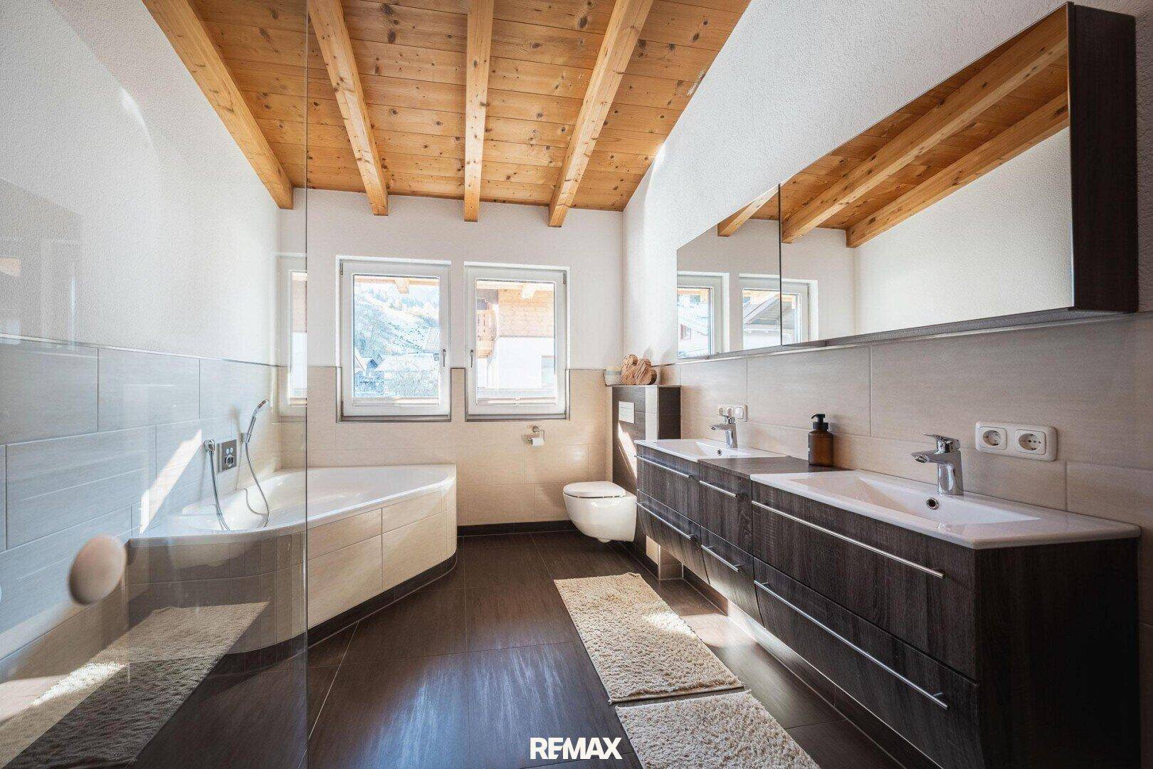 Modernes Badezimmer mit Eckbadewanne, Doppelwaschbecken und Holzbalkendecke.