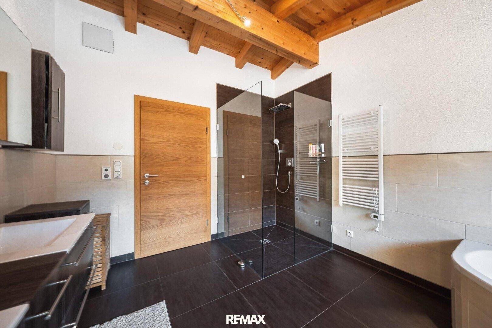 Modernes Badezimmer mit begehbarer Dusche, Handtuchheizkörper und Holzbalkendecke.