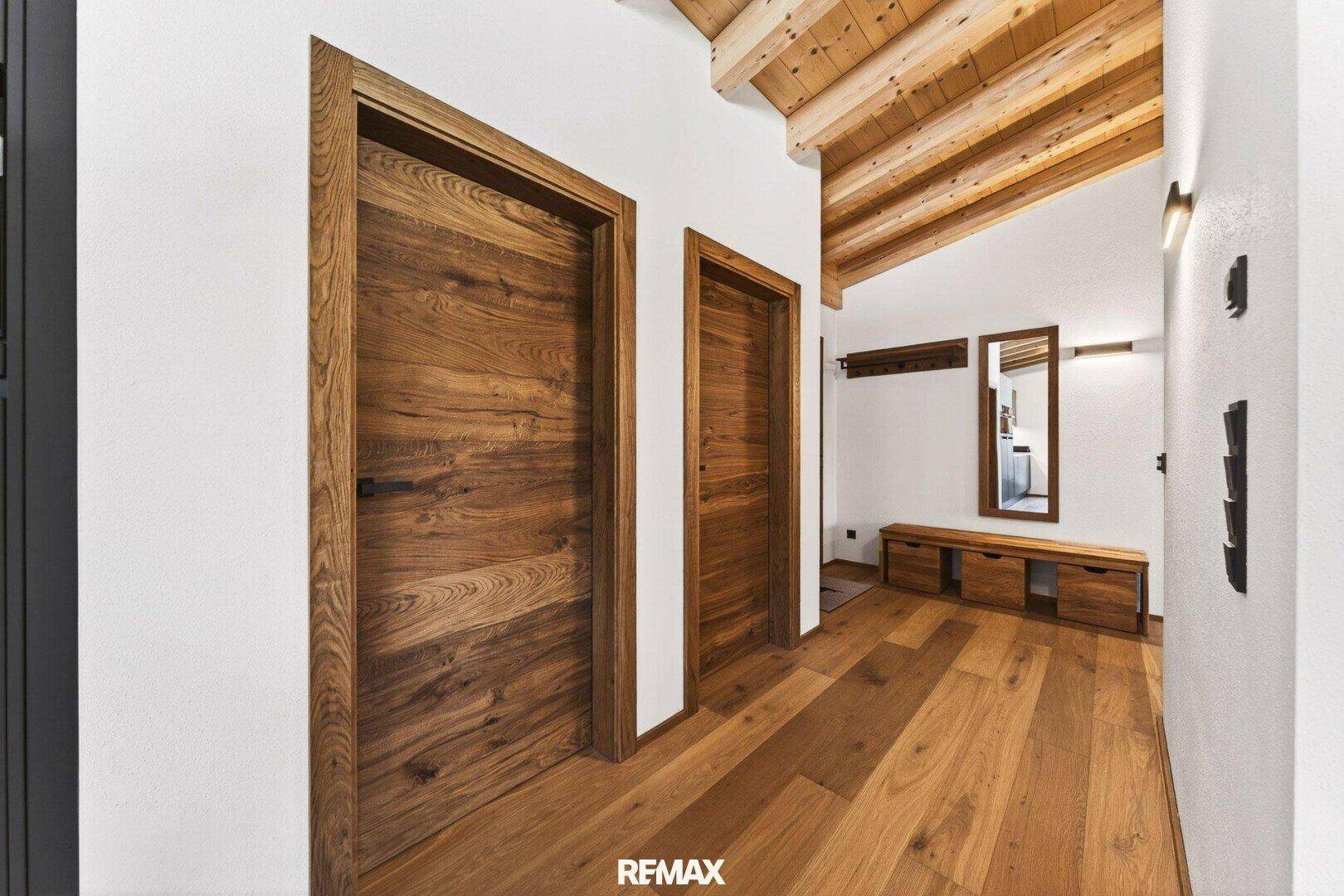 Heller Flur mit Holztüren, Holzboden und einer Sitzbank mit Spiegel.