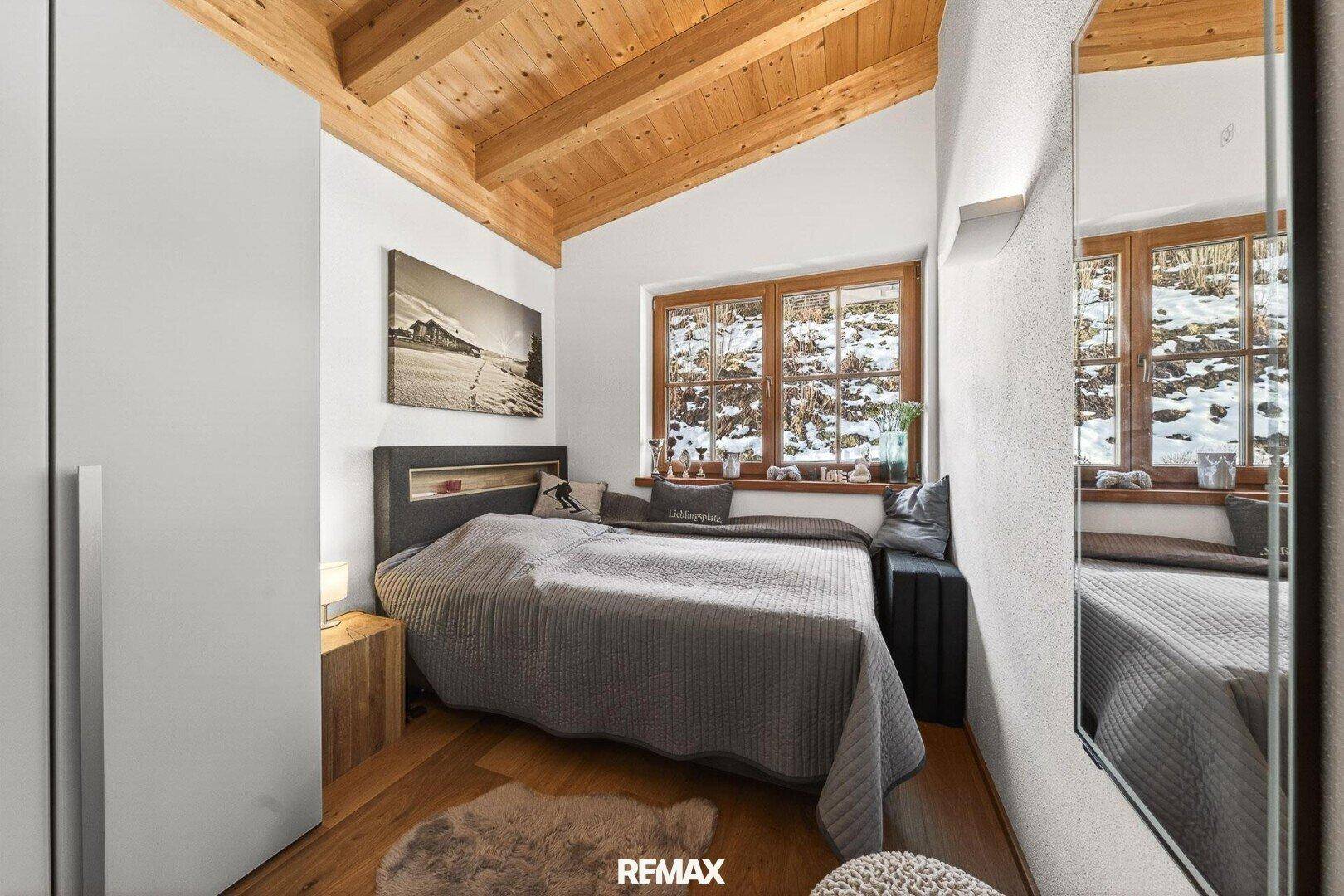 Helles Schlafzimmer mit Holzbalkendecke, Holzboden und Blick auf die verschneite Landschaft.