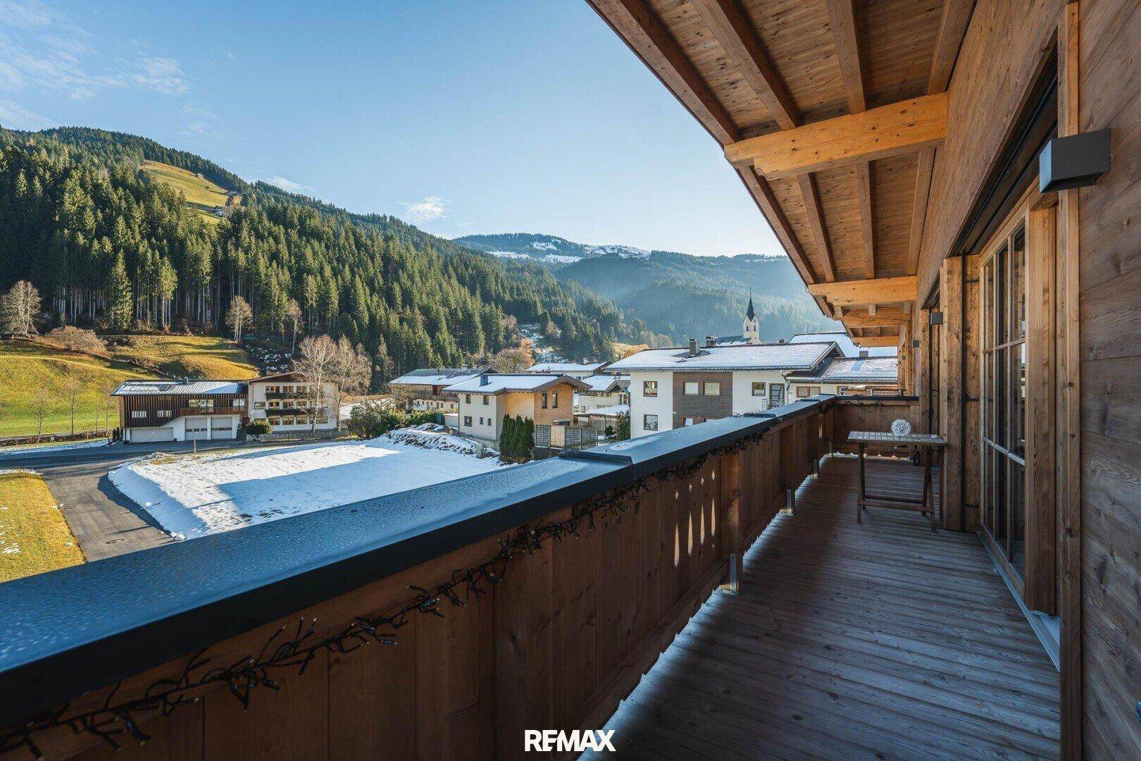 Geräumiger Holzbalkon mit Blick auf die verschneite Berglandschaft und das Dorf.