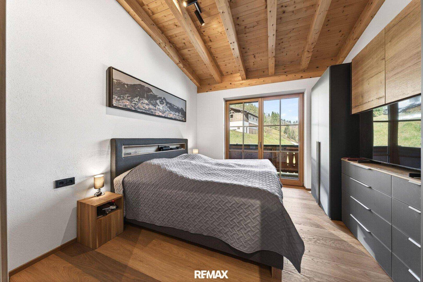 Schlafzimmer mit Holzbalkendecke, Holzboden und Zugang zu einem Balkon mit Bergblick.