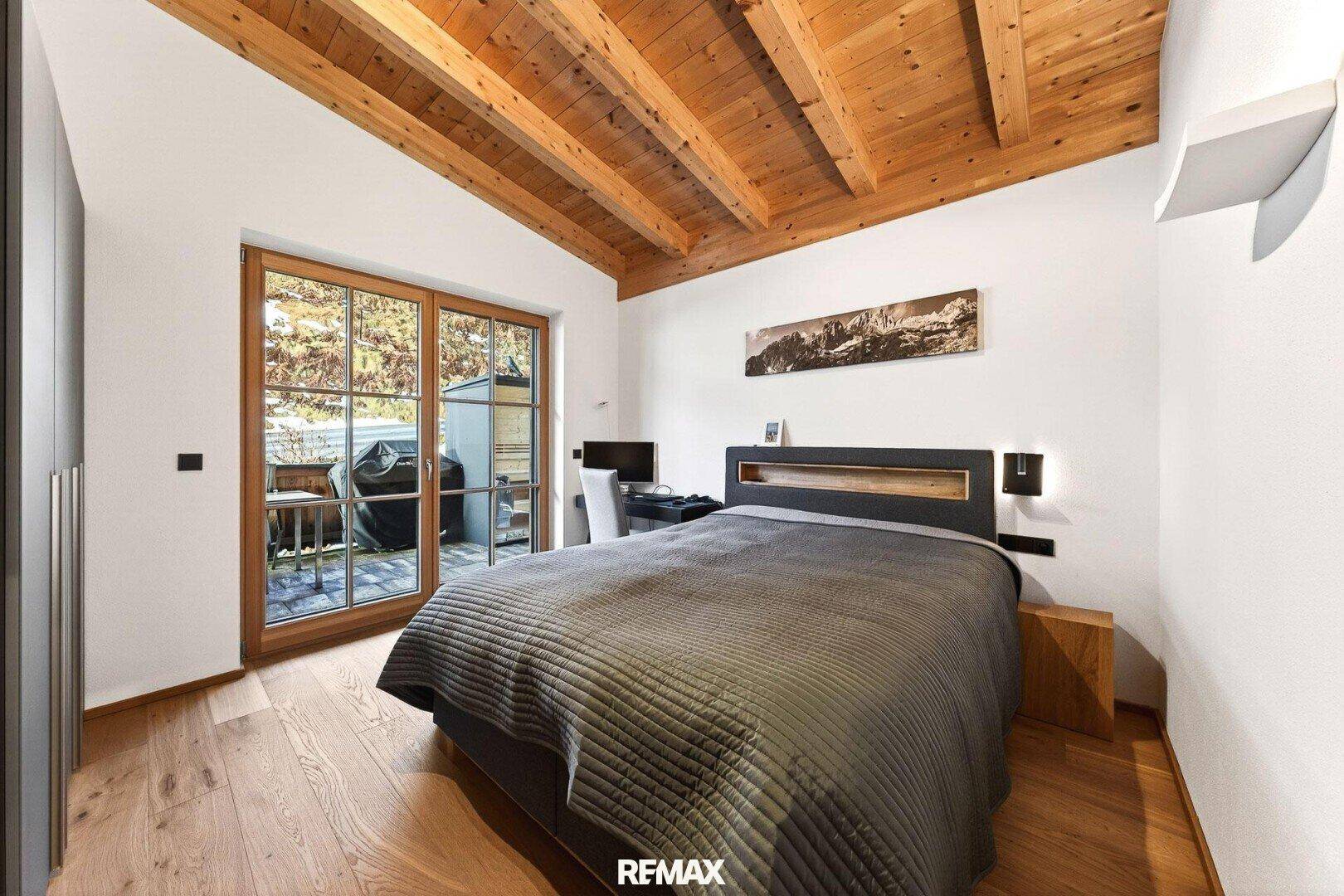 Gemütliches Schlafzimmer mit Holzbalkendecke, Holzboden und Zugang zur Terrasse.