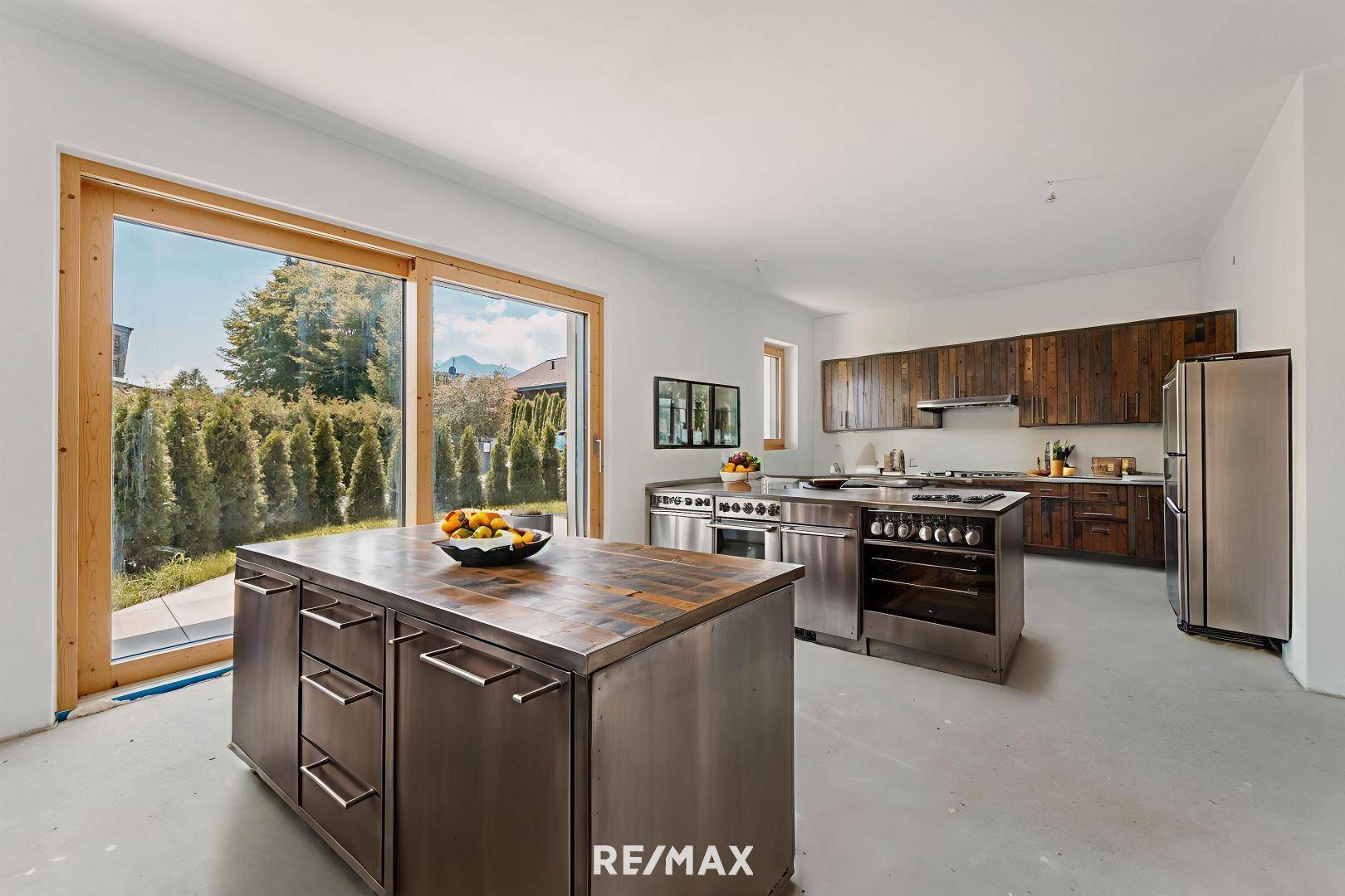 Geräumige Küche mit zwei Kücheninseln, modernen Edelstahlgeräten und Zugang zum grünen Garten.