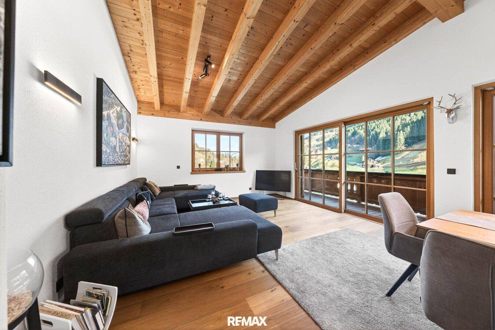 Gemütliches Wohnzimmer mit großem Sofa, Holzbalkendecke und Zugang zum Balkon.