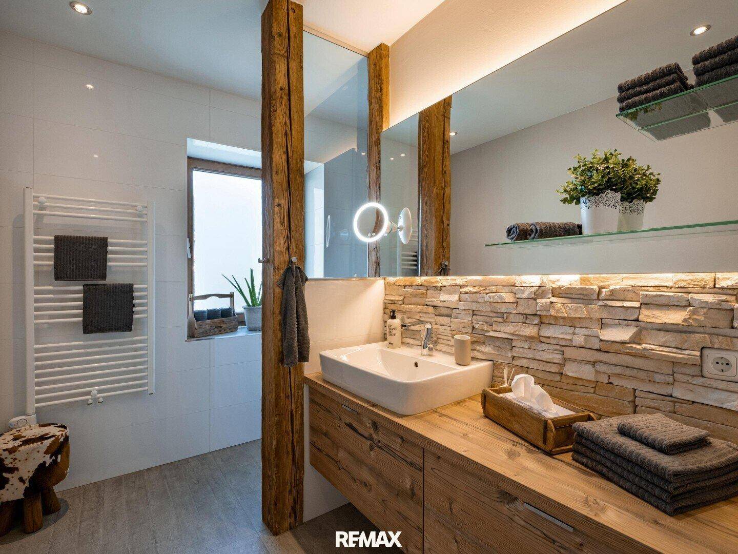 Stilvolles Badezimmer mit Holzwaschtisch, Natursteinwand, beheiztem Handtuchhalter und Holzbalken.