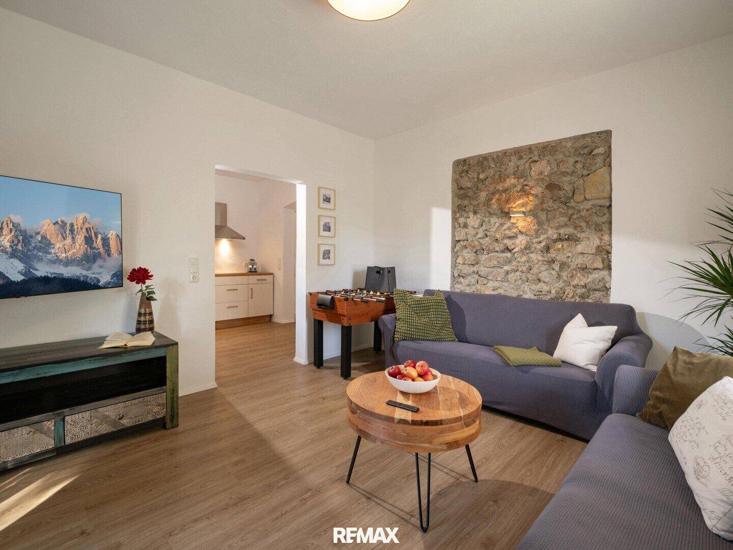 Helles Wohnzimmer mit Steinwand, bequemen Sofas und einem Tischfußballspiel, ideal für Unterhaltung.