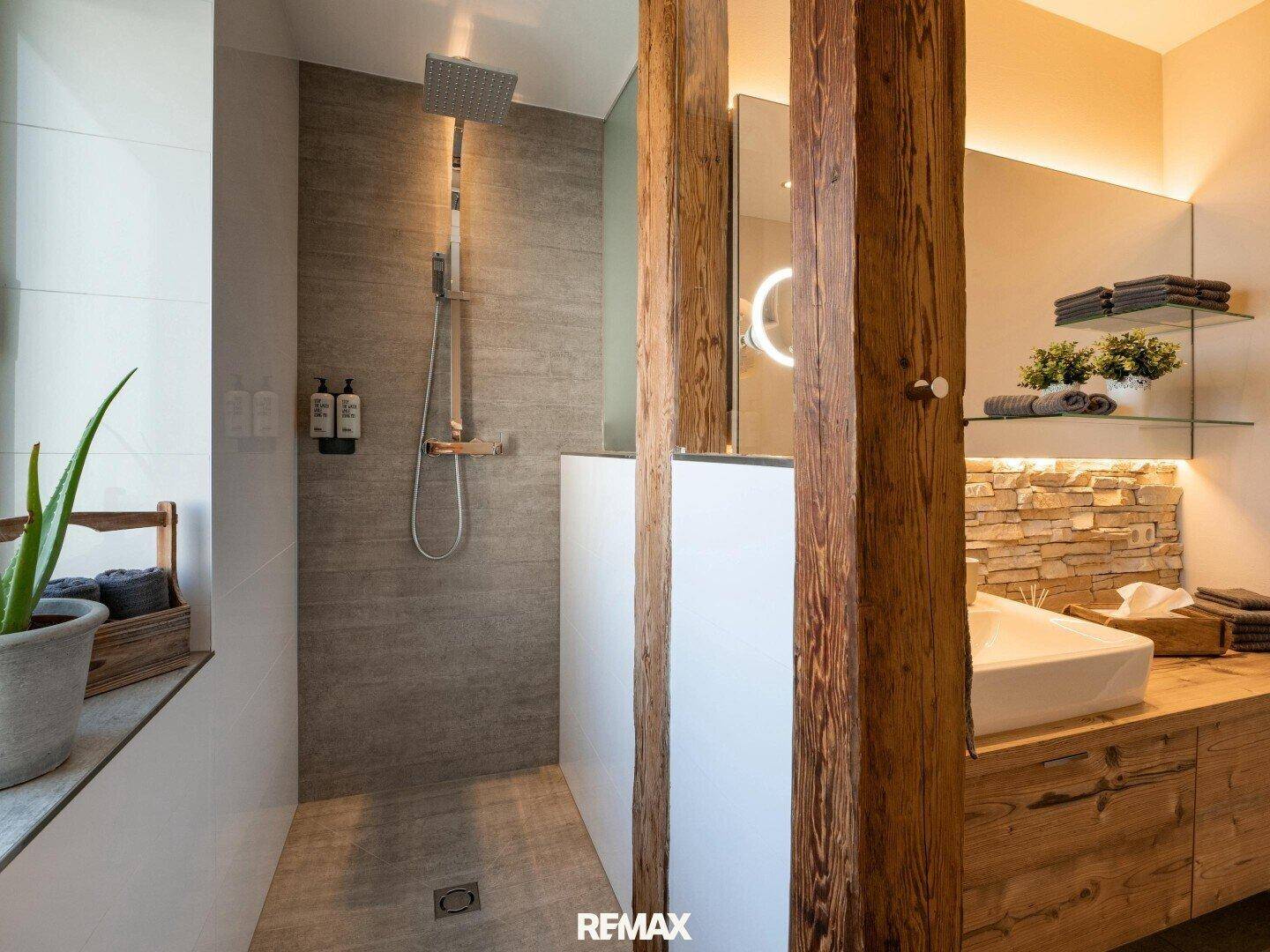 Modernes Badezimmer mit begehbarer Dusche, Holzwaschtisch und Natursteinwand, mit sichtbaren Holzbalken.