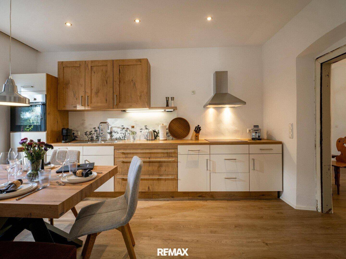 Moderne Küche mit Holz- und weißen Fronten, integrierten Geräten und einem Esstisch im Vordergrund.
