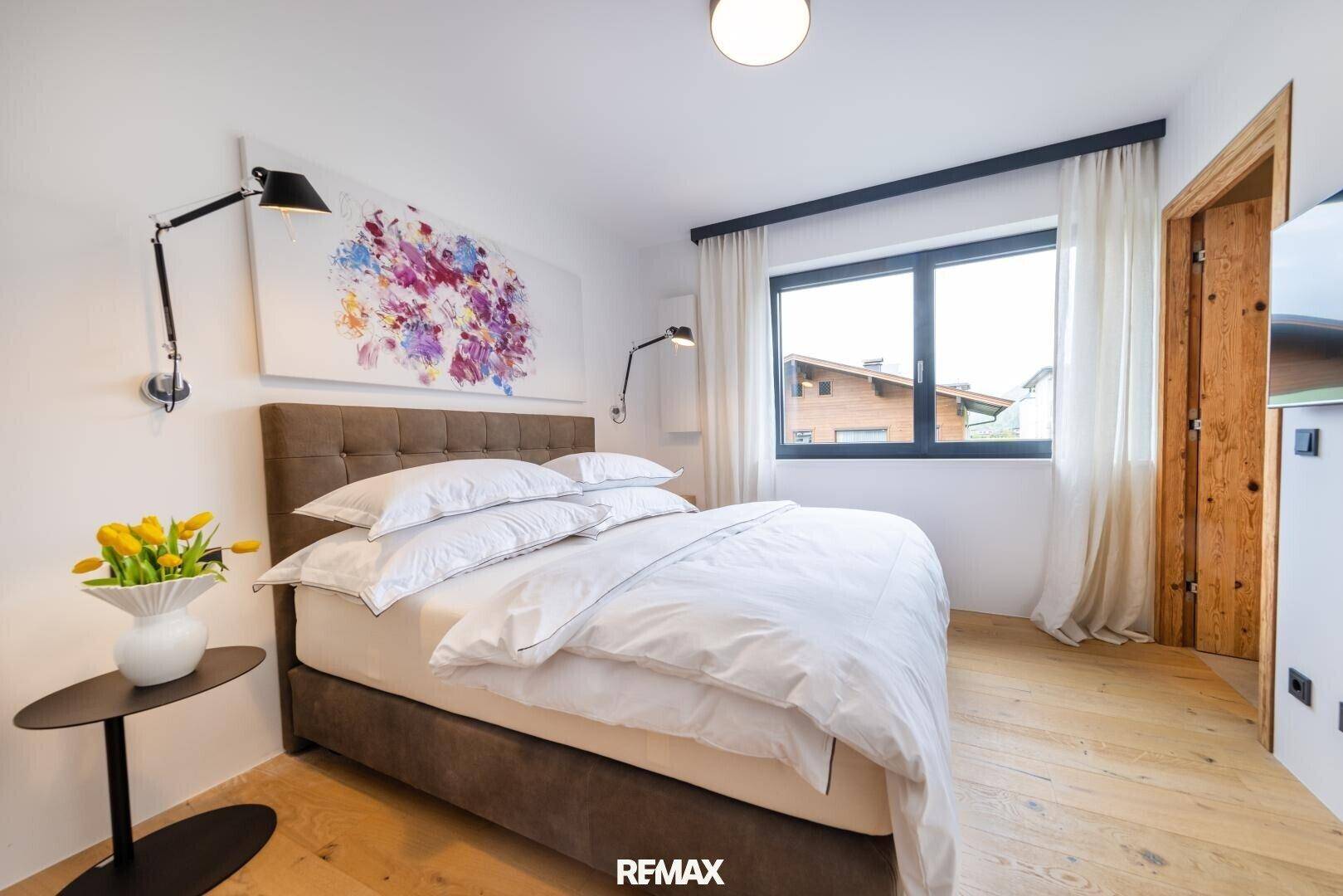 Helles Schlafzimmer mit großem Fenster, Holzboden und stilvoller Einrichtung.