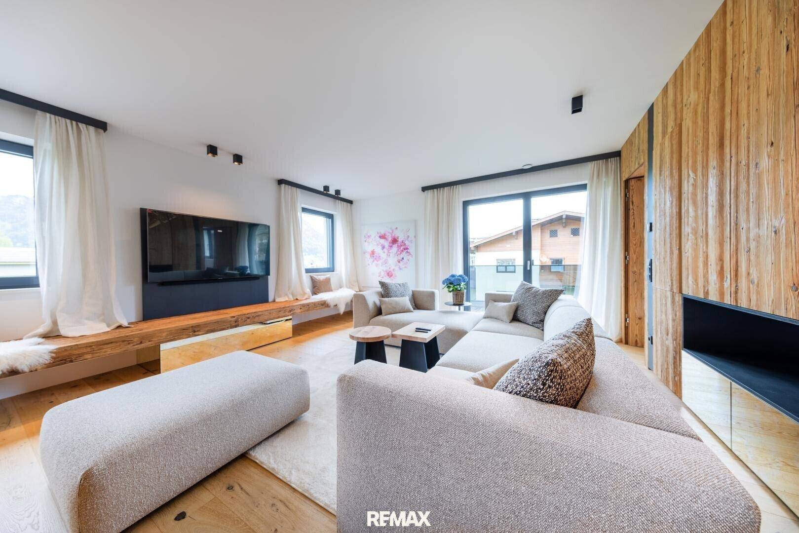Helles Wohnzimmer mit großem Ecksofa, Holzwand und Zugang zu einem Balkon oder Terrasse.