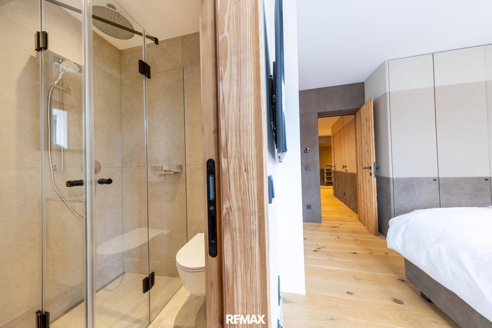 Modernes Badezimmer mit begehbarer Regendusche, Wand-WC und Holzelementen, direkt vom Schlafzimmer zugänglich.