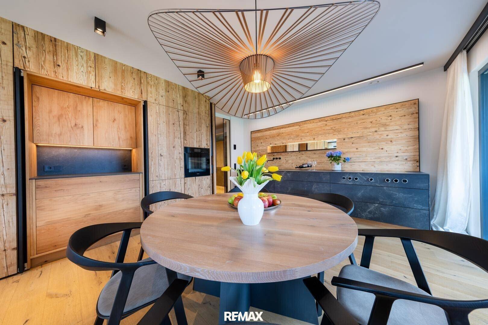 Moderne Küche mit Holzwänden, integrierten Geräten und einem runden Esstisch unter einer Designerlampe.