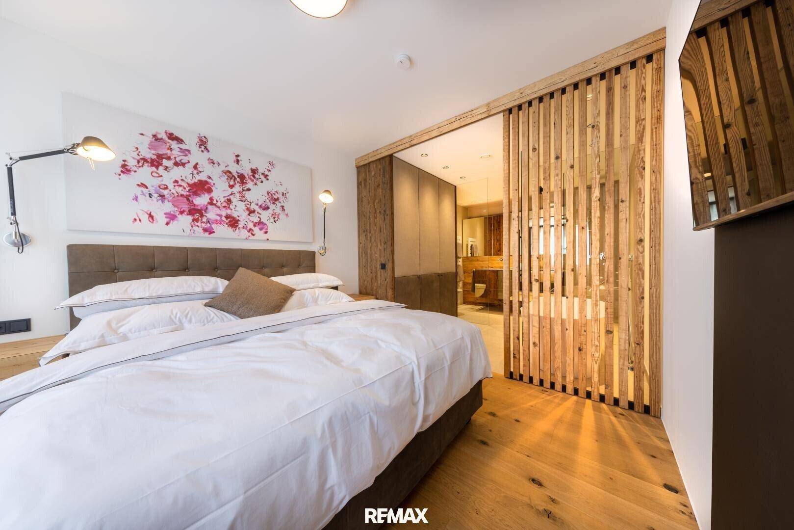 Modernes Schlafzimmer mit Holzboden, großem Bett und Schiebetür zum angrenzenden Badezimmer.