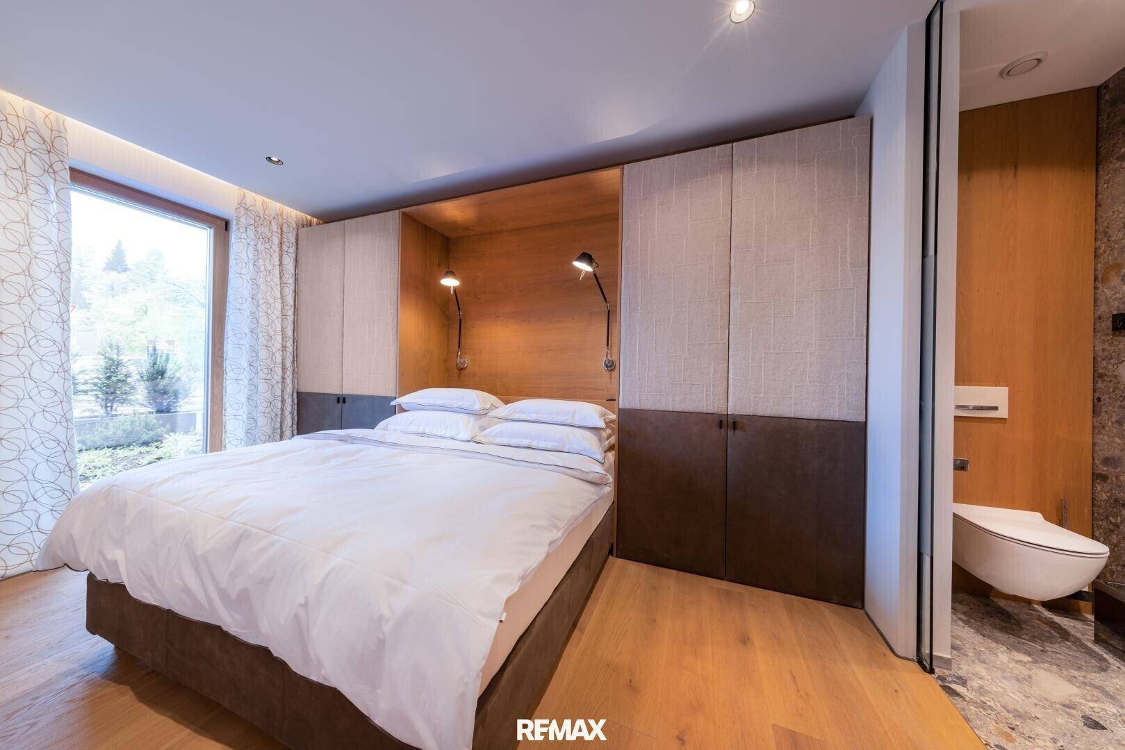 Komfortables Schlafzimmer mit großem Bett, Einbauschränken und Fenster mit Blick ins Grüne.