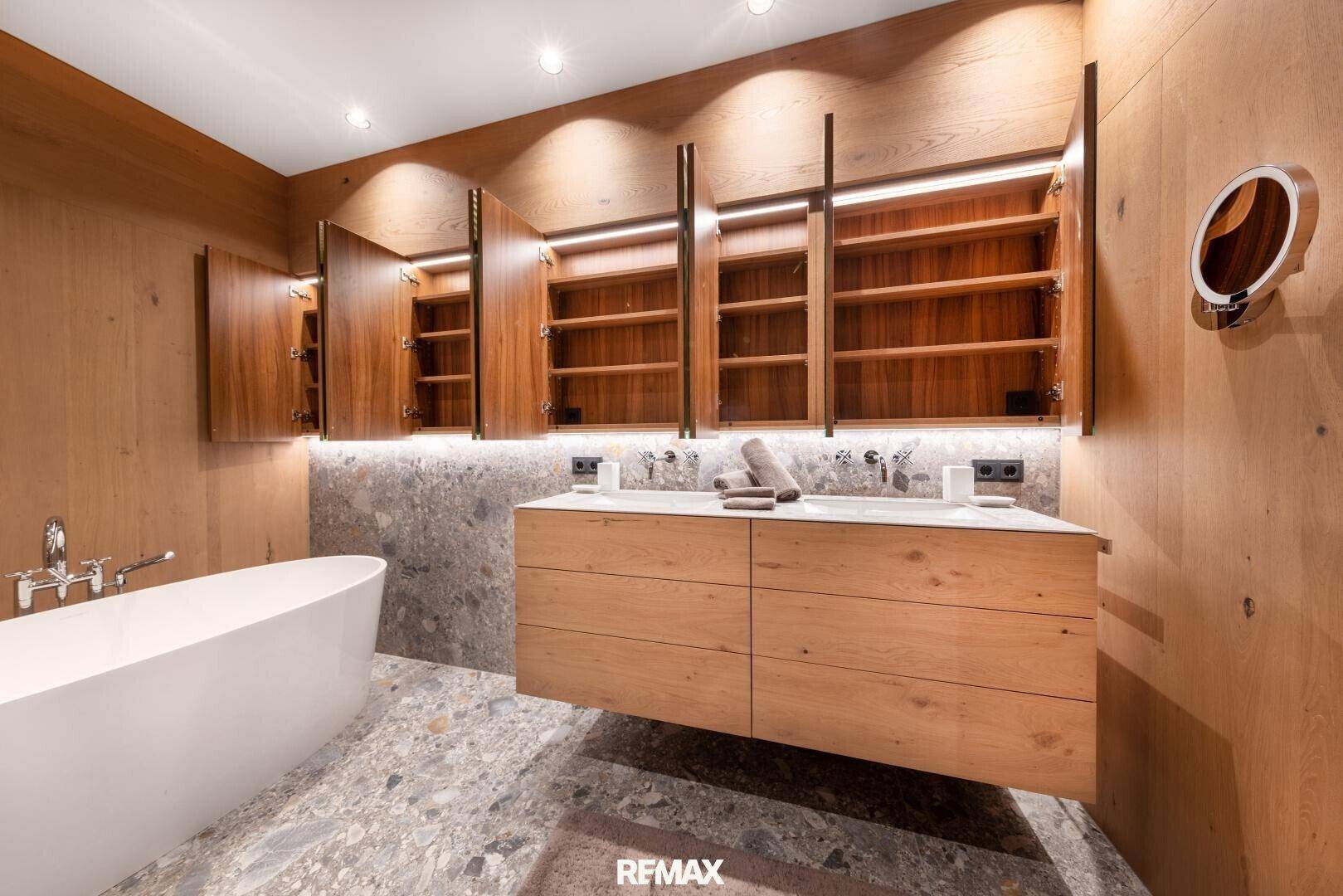 Elegantes Badezimmer mit Doppelwaschbecken, beleuchteten Spiegelschränken und freistehender Badewanne.