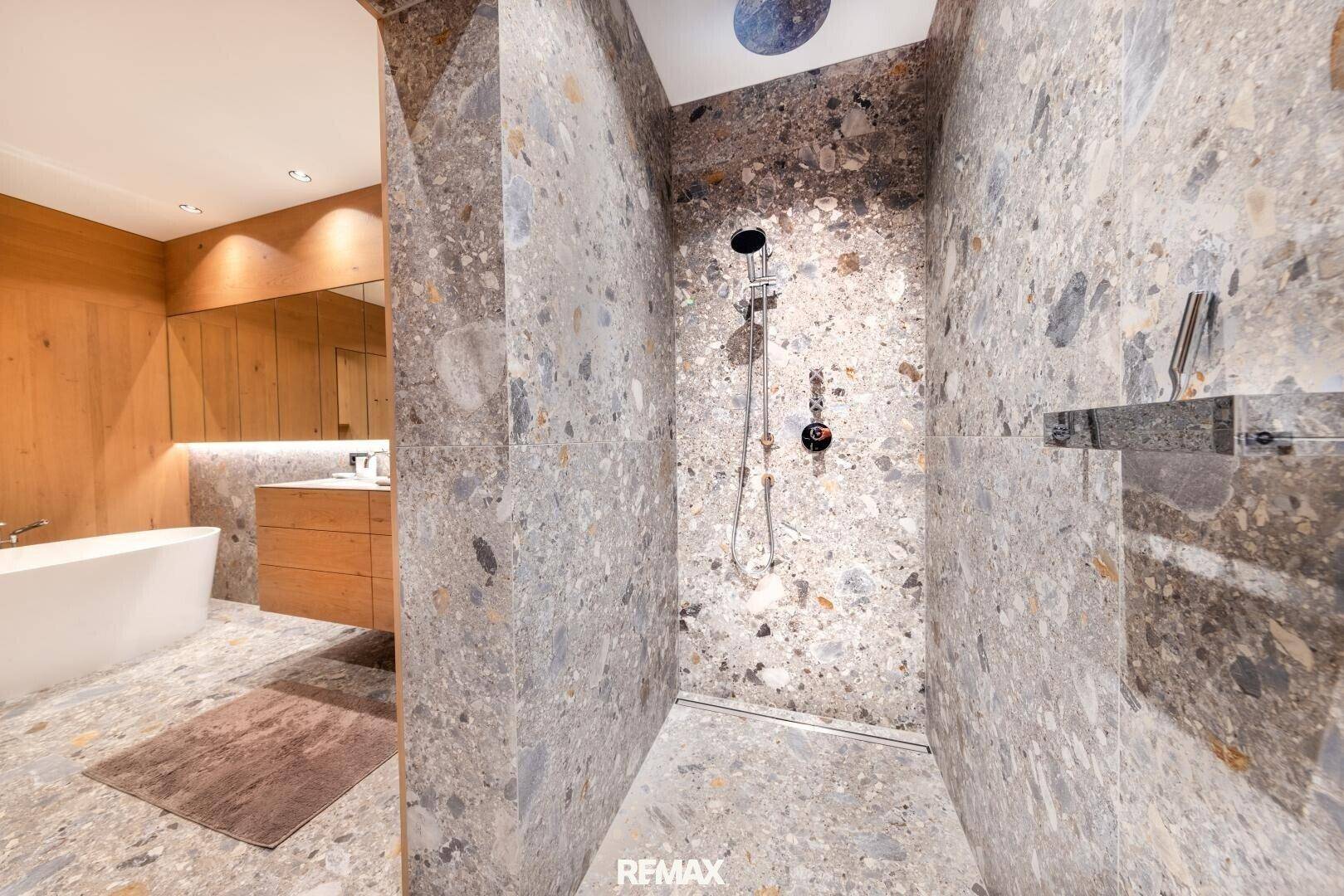 Geräumige begehbare Dusche mit Regenduschkopf und modernen Steinfliesen im Badezimmer.