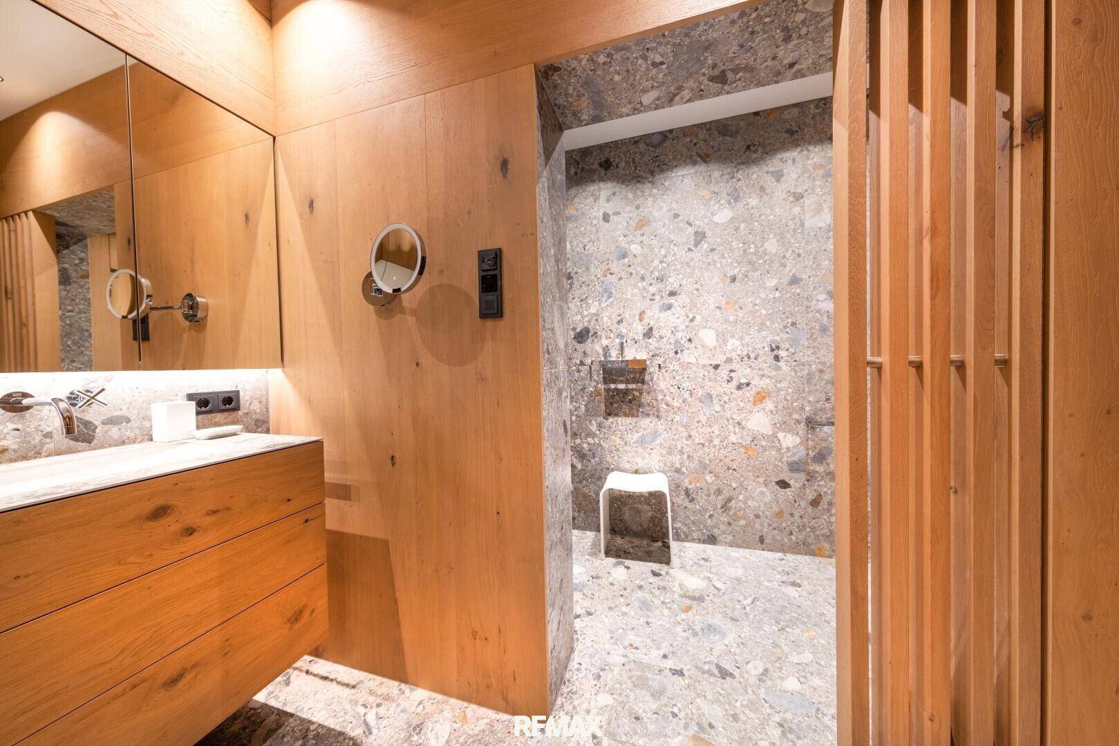 Modernes Badezimmer mit begehbarer Dusche, Steinwänden und Holzdetails.