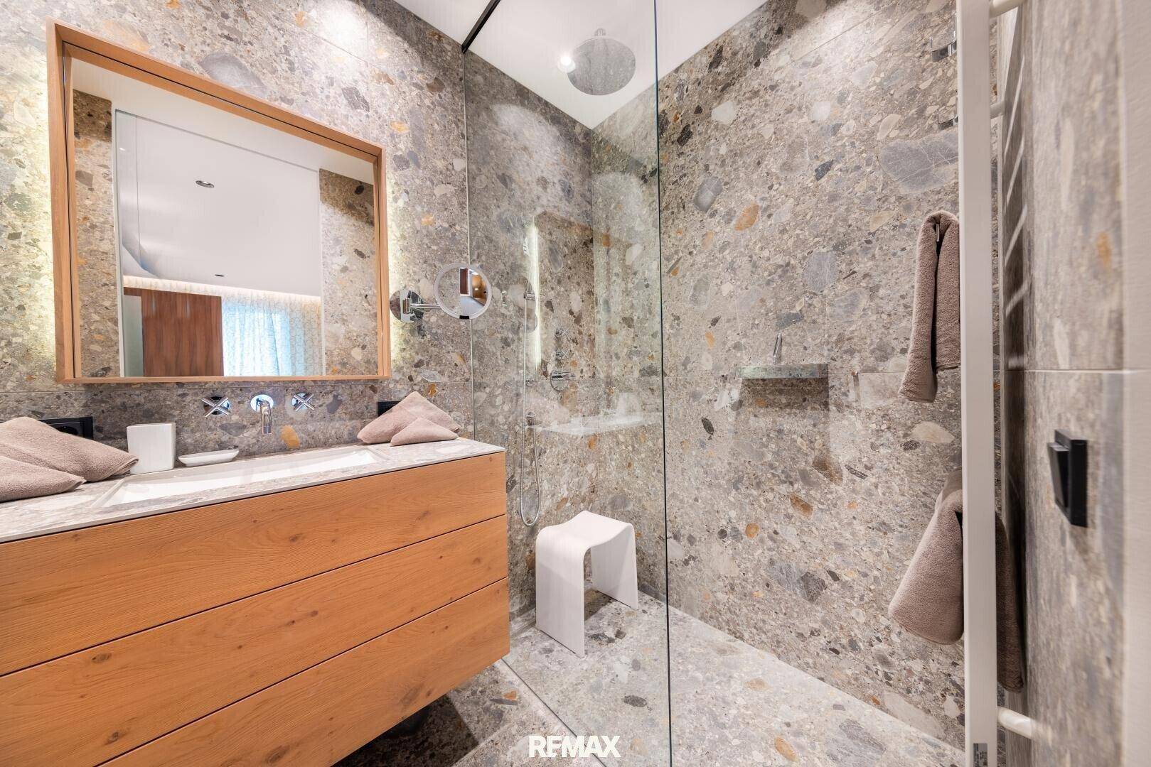 Elegantes Badezimmer mit großer begehbarer Dusche, modernen Armaturen und Natursteinfliesen.