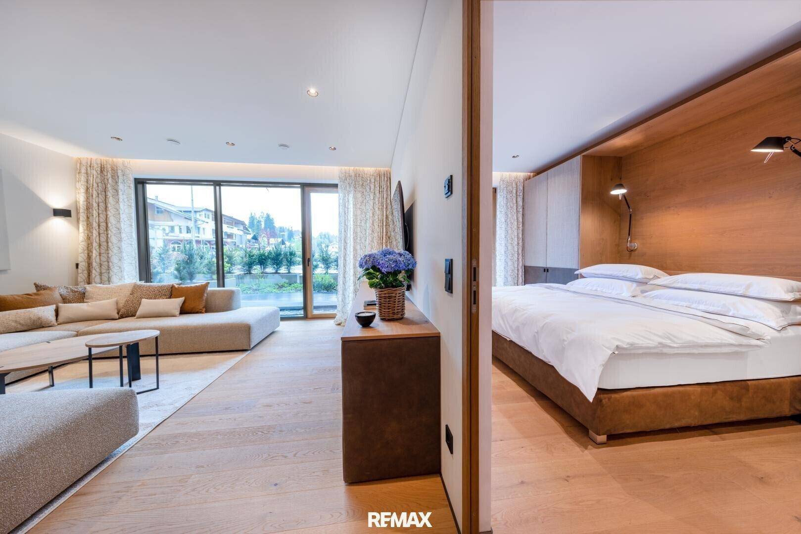 Gemütlicher Wohnbereich mit bequemer Couch, Holzboden und Zugang zu einem Schlafzimmer.