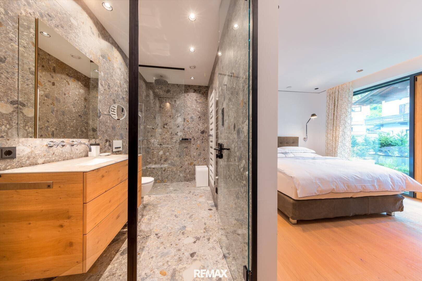 Elegantes Badezimmer mit Steinfliesen, Holzwaschtisch und großer Dusche, verbunden mit dem Schlafzimmer.