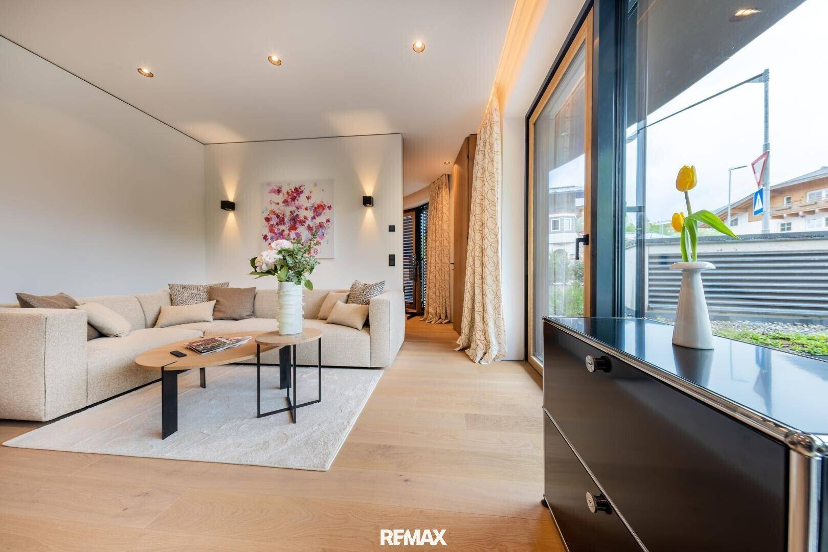 Helles, modernes Wohnzimmer mit beigem Sofa, Holzboden und Zugang zu einem Außenbereich.