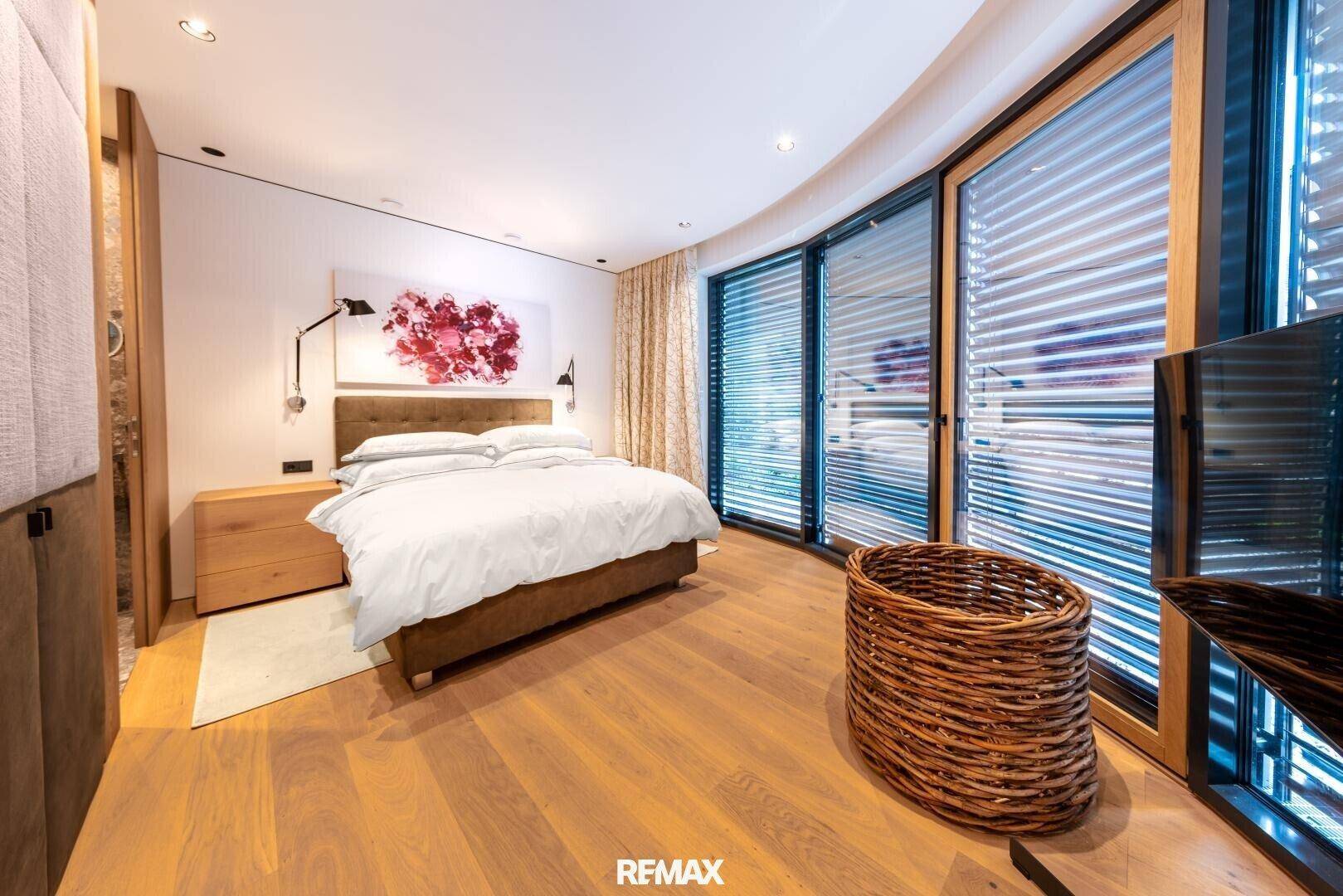 Helles Schlafzimmer mit Holzboden, bequemen Bett und großen, gebogenen Fenstern für viel Licht.