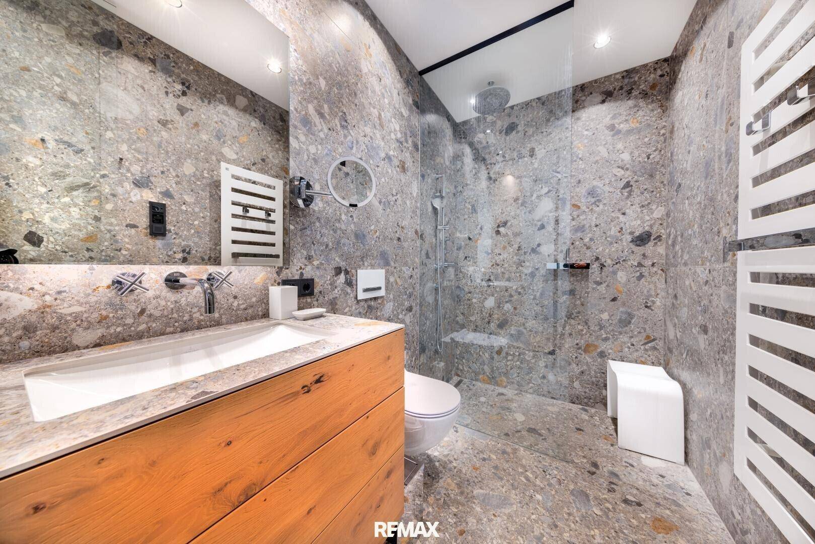 Stilvolles Badezimmer mit begehbarer Dusche, modernen Armaturen und Steinfliesen an Wänden und Boden.