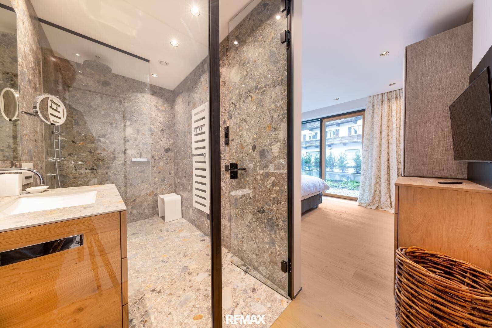 Modernes Badezimmer mit begehbarer Dusche, Steinfliesen und Holzwaschtisch, direkt vom Schlafzimmer zugänglich.