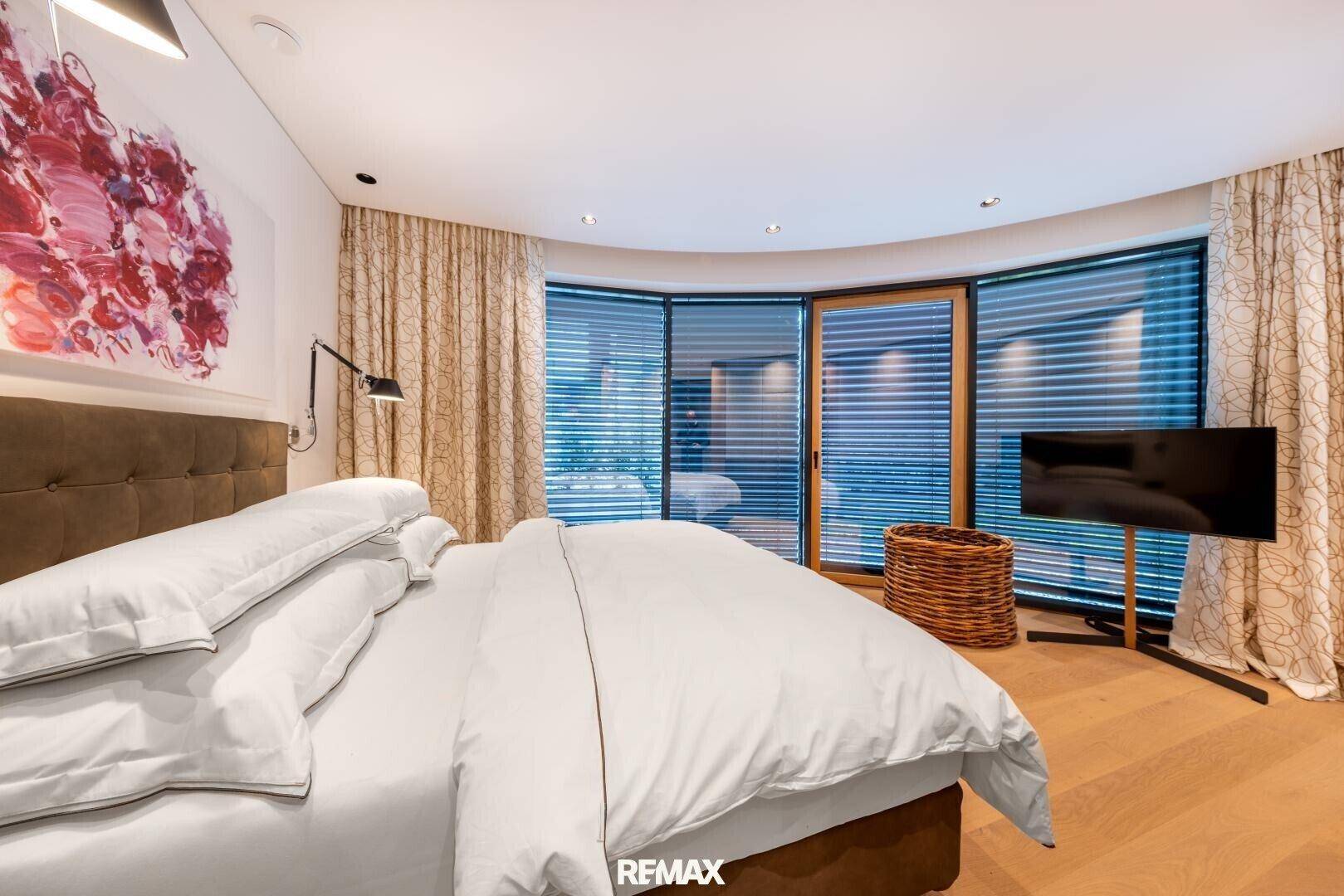 Gemütliches Schlafzimmer mit großem Bett, Holzboden und raumhohen Fenstern mit Jalousien.