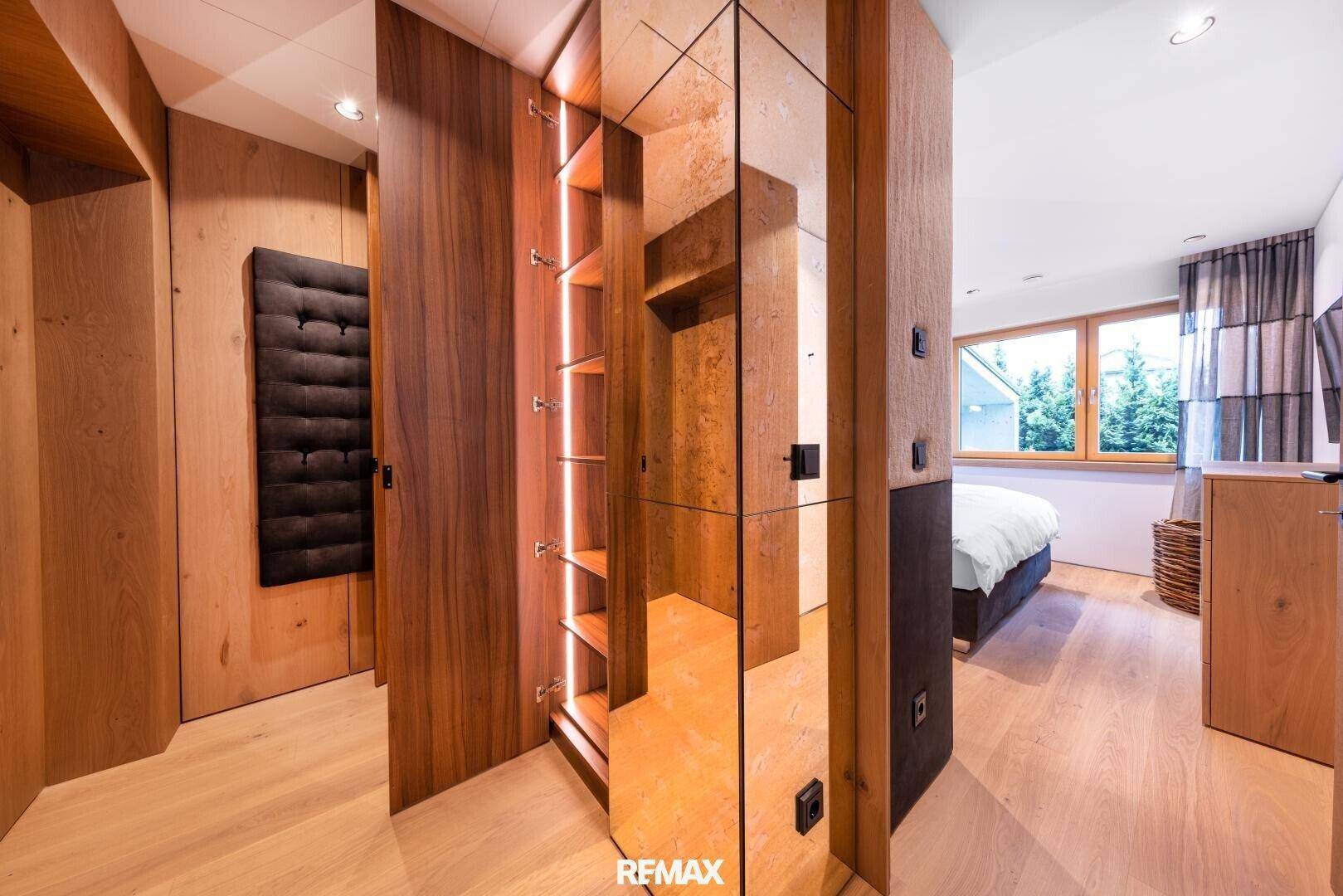 Offener Schlafbereich mit begehbarem Kleiderschrank und Holzelementen. Spiegelnde Oberflächen erweitern den Raum optisch.