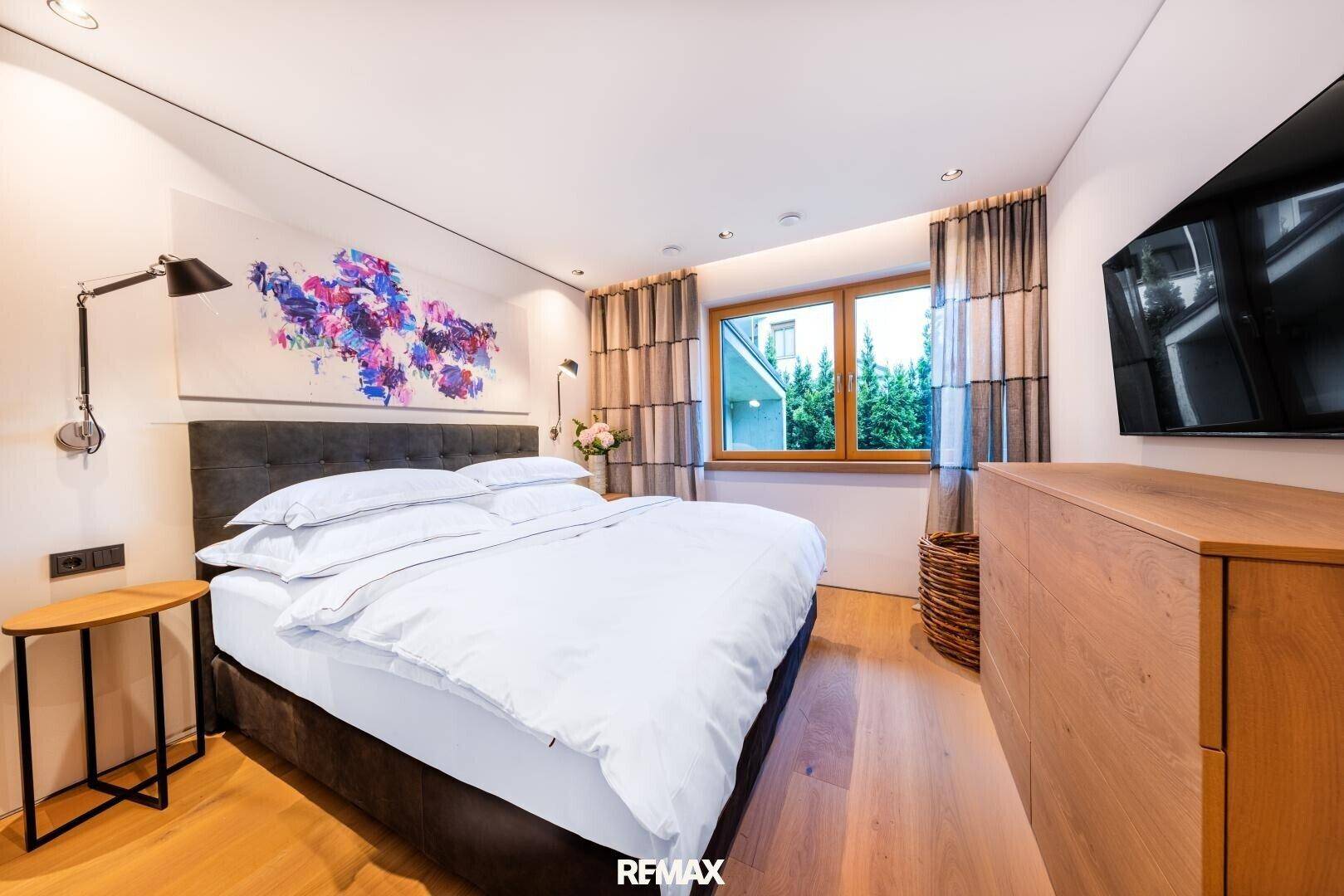 Helles Schlafzimmer mit großem Bett, Holzboden und Blick ins Grüne. Ein Flachbildfernseher ist an der Wand montiert.