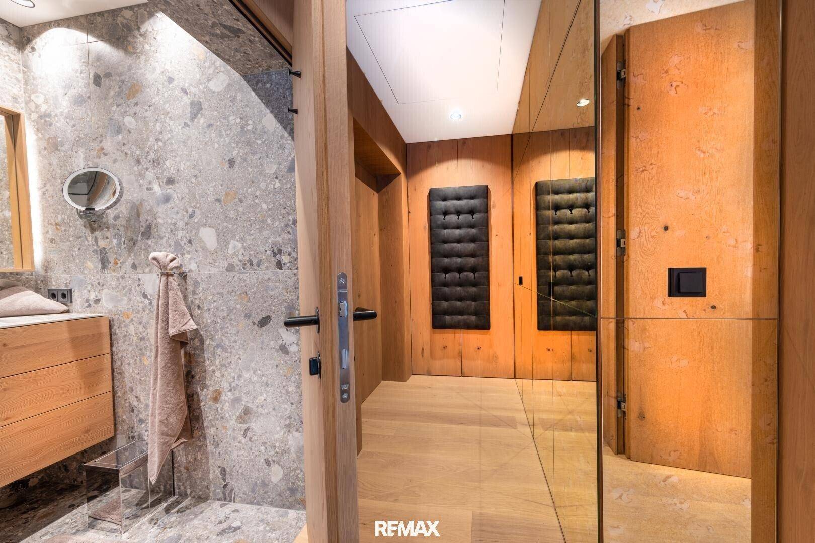 Eingangsbereich zum modernen Badezimmer mit Holztür und Steinwand. Ein Spiegel reflektiert den Raum.