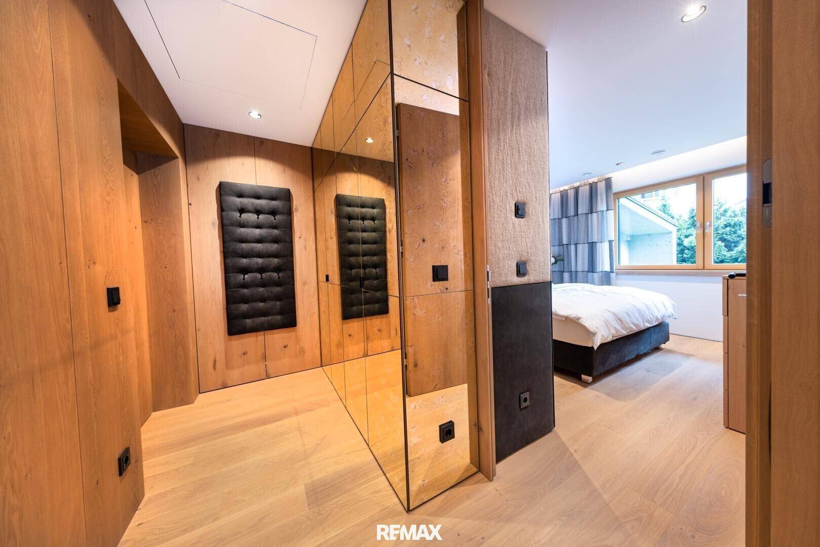 Schlafzimmer mit Holzwänden, Spiegelfronten und Zugang zu einem weiteren Raum.