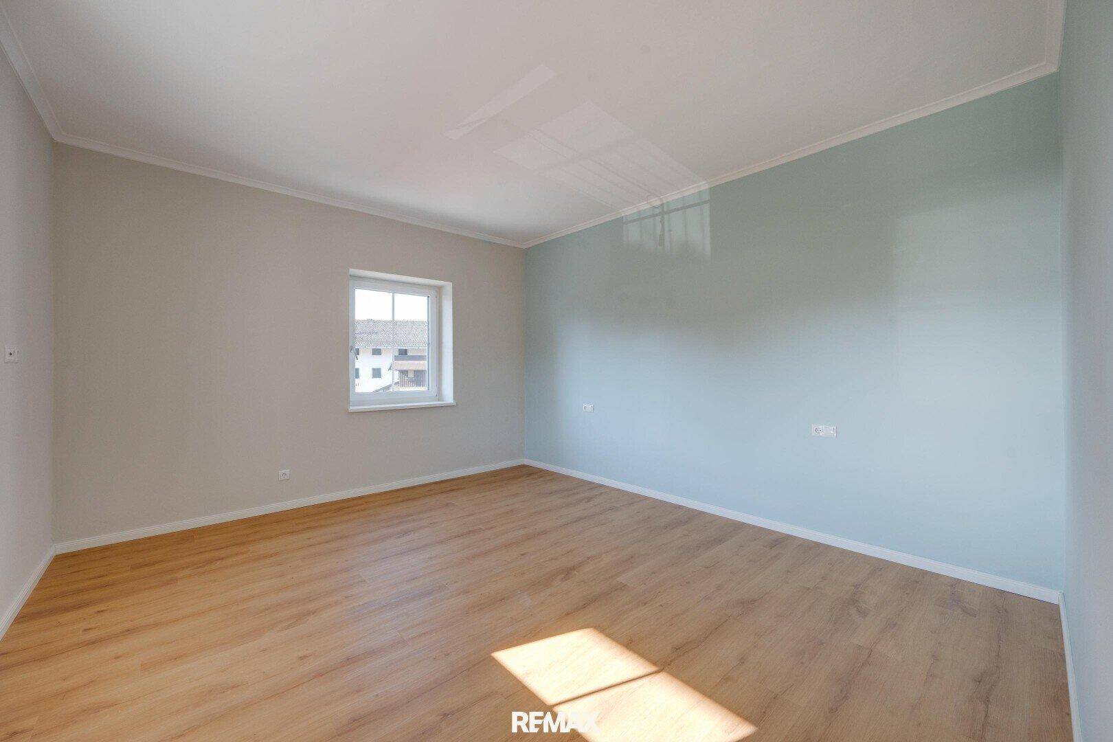 Leerer Raum mit hellem Laminatboden und Fenster, bereit zur individuellen Gestaltung und Nutzung.