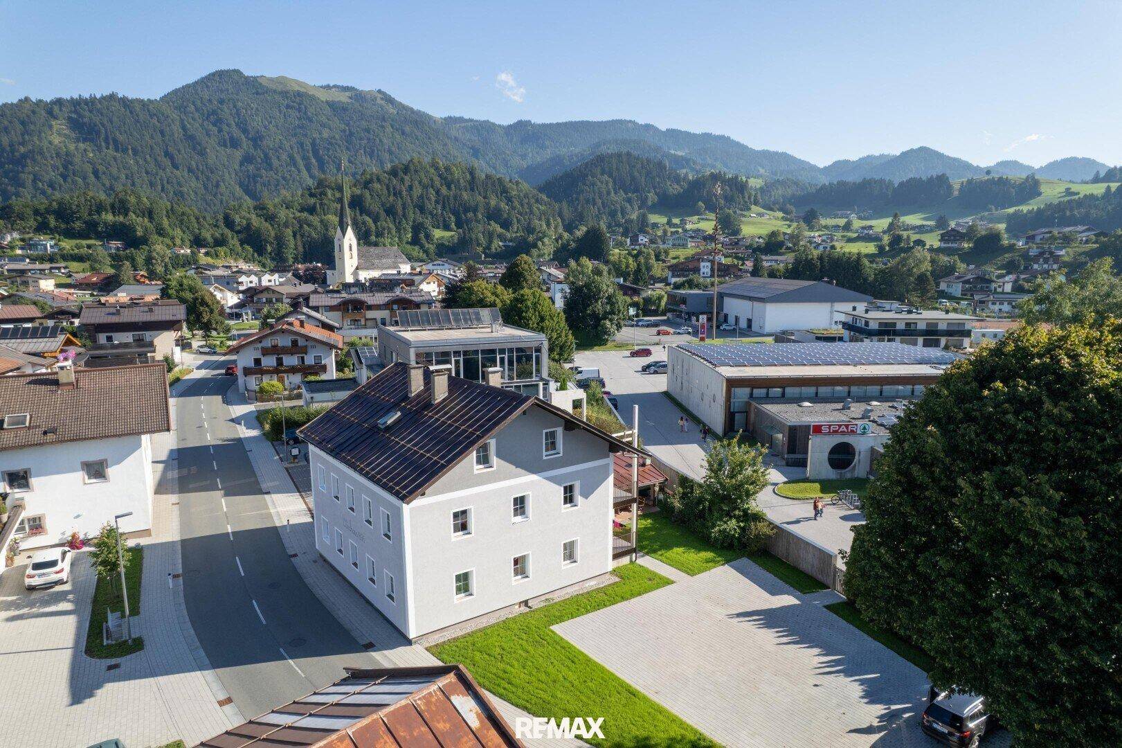 Luftaufnahme eines Wohnhauses mit Photovoltaikanlage in einer ländlichen Umgebung mit Bergen.