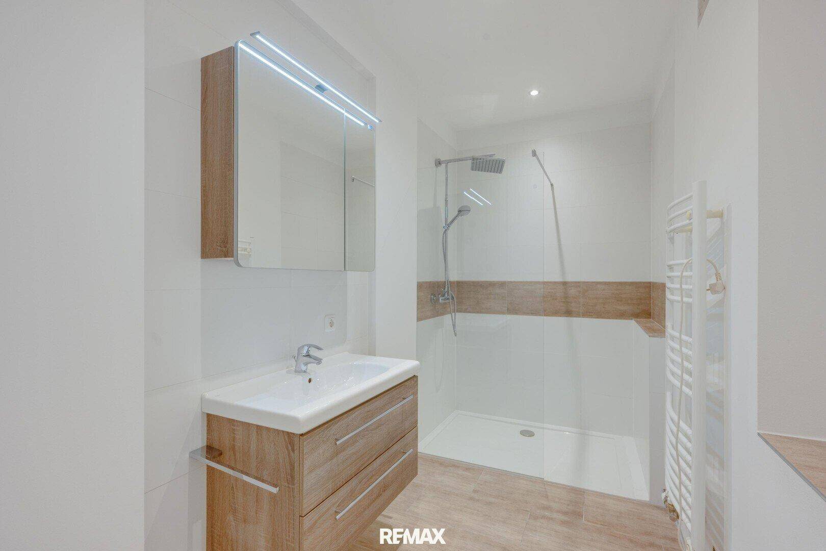 Modernes Badezimmer mit begehbarer Dusche, Holzoptik-Waschtisch und einem praktischen beheizten Handtuchhalter.