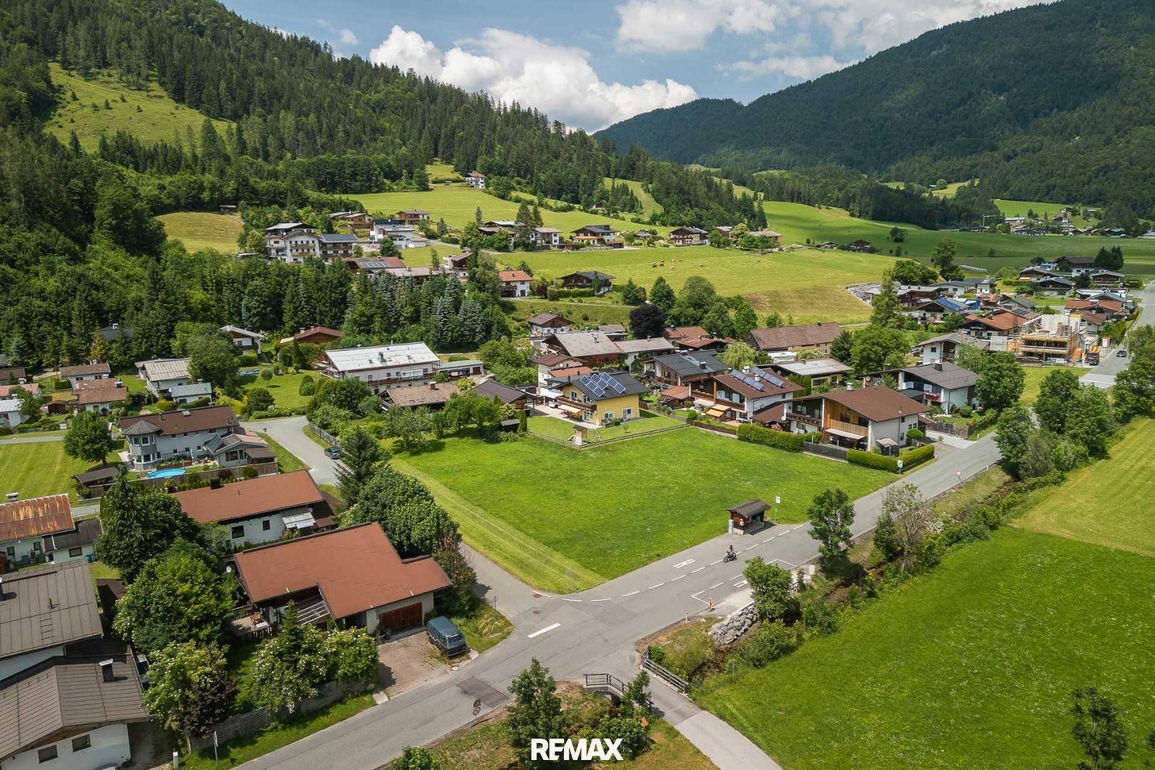 Panoramablick auf eine idyllische Siedlung in einem grünen Tal, umgeben von bewaldeten Bergen.