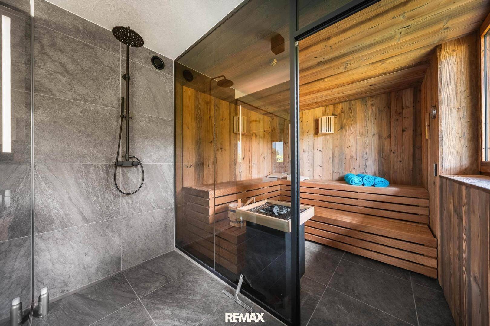 Modernes Badezimmer mit Dusche und integrierter Sauna, gefliest in dunklem Grau.