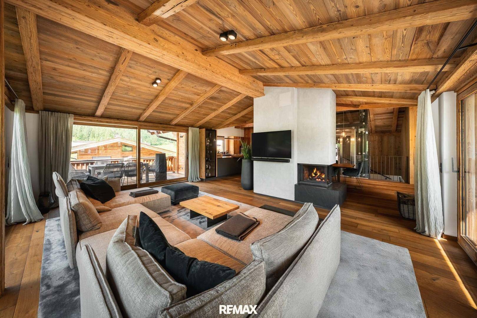 Gemütliches Wohnzimmer mit Kamin, Holzbalkendecke und Zugang zum Balkon.
