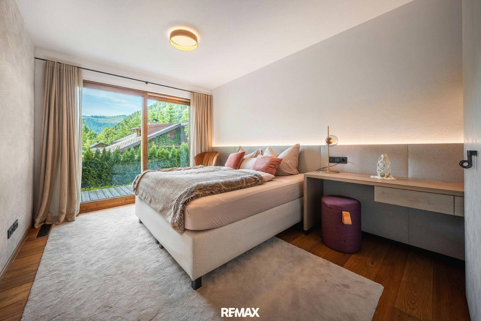 Helles Schlafzimmer mit großem Fenster, Doppelbett und Schreibtisch mit Bergblick.